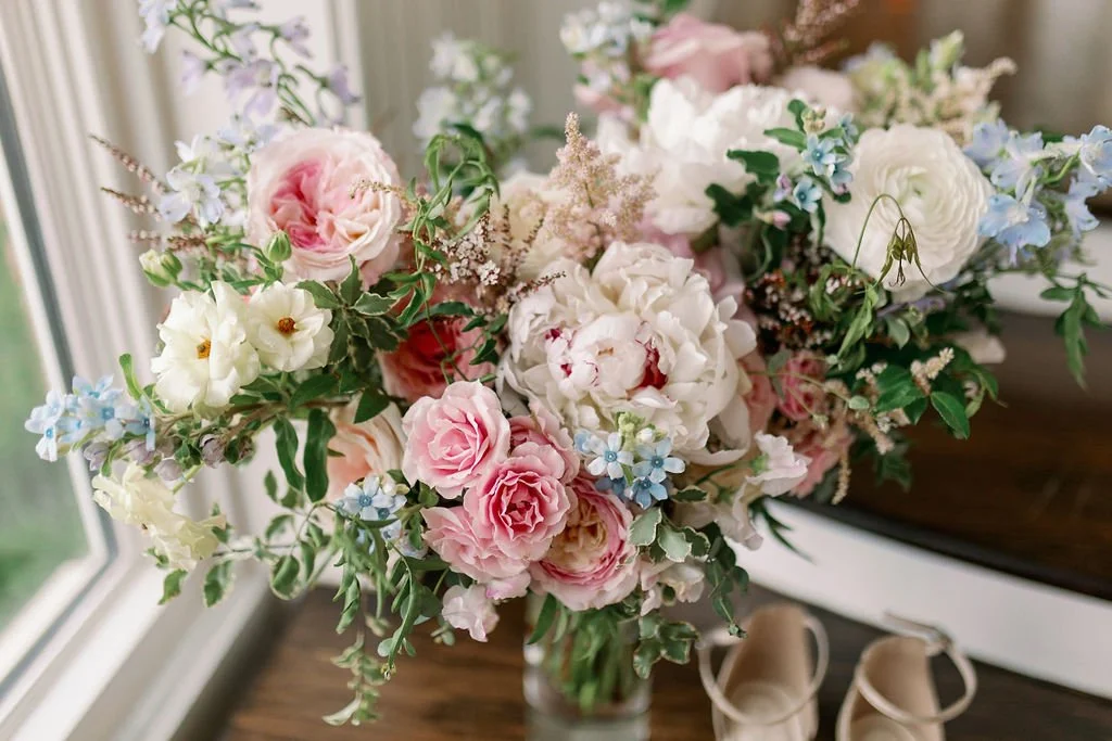 A lush bridal bouquet filled with hues of blush, pink, ivory, and hints of French blue. Garden roses, majolica spray roses, champagne roses, peonies, ranunculus, delphinium, and spirea make up this fairytale bouquet. Designed by Rosemary & Finch in N