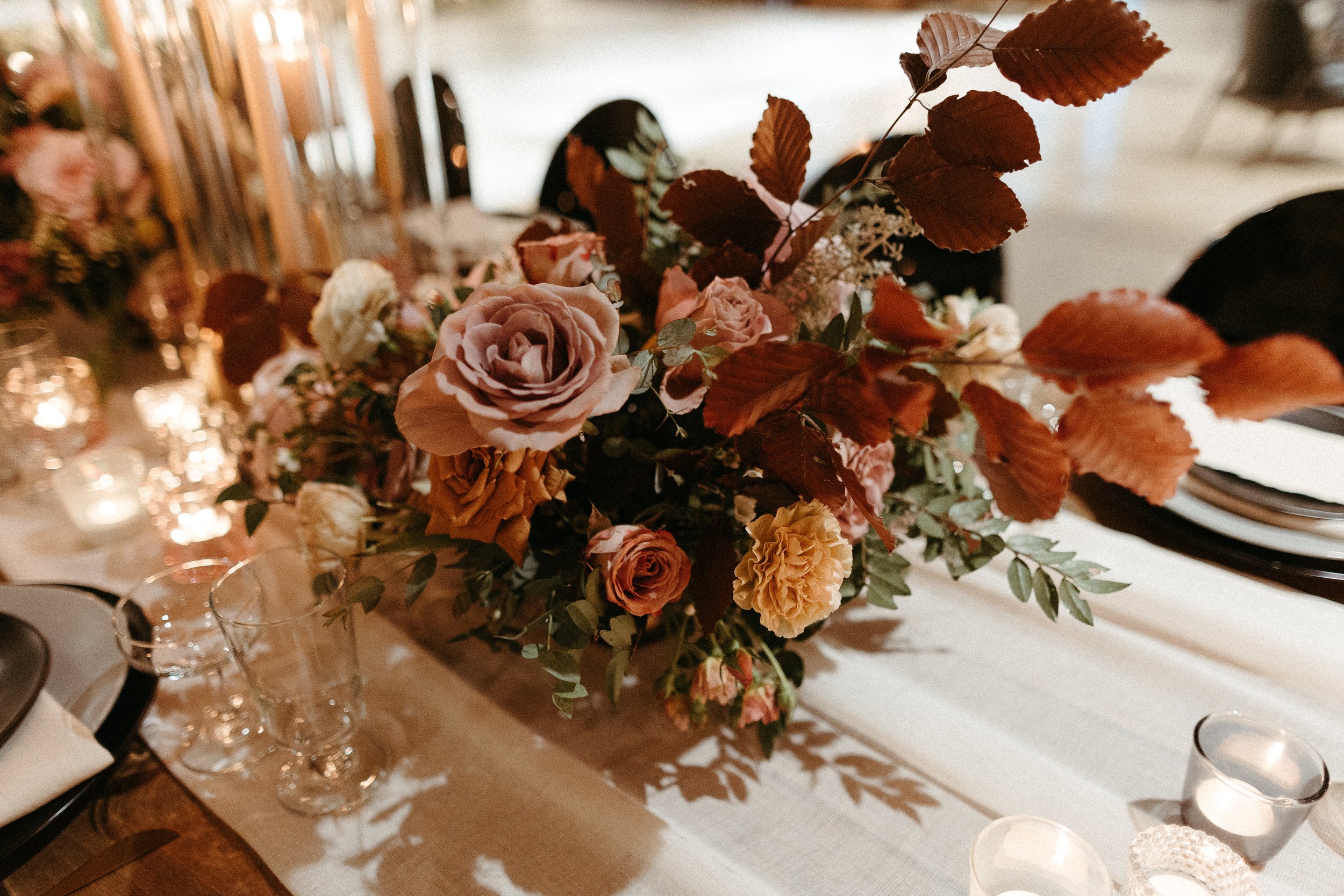 Gorgeous centerpieces bring warmth to this art deco 1920s inspired wedding with hues of terra cotta, dusty pink, mauve, and burgundy. Lush roses, ranunculus, and copper beech highlight the florals. Designed by Rosemary and Finch in Nashville, TN.
