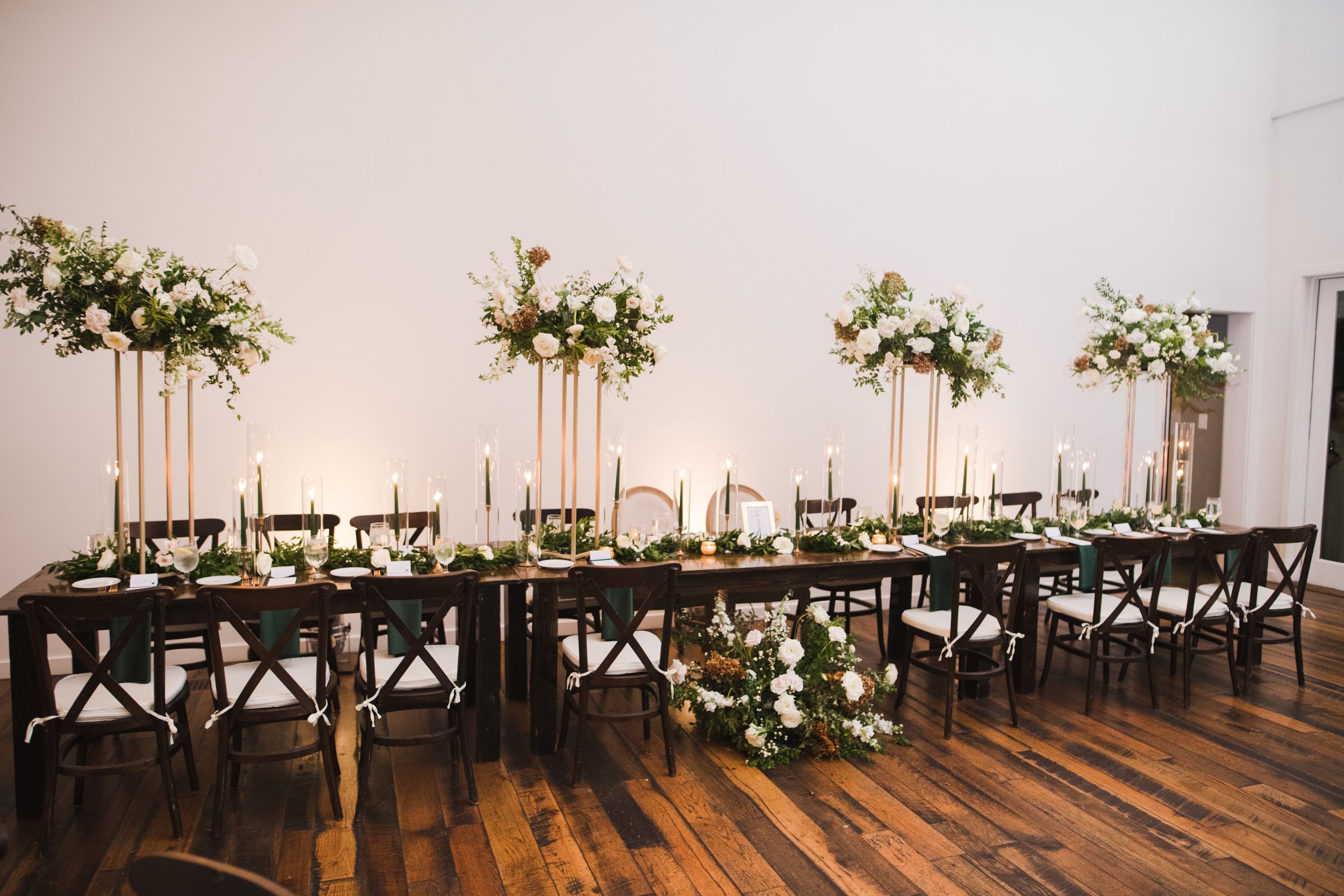 Elevated gold stands with lush floral centerpieces of white garden roses, ranunculus, snapdragons, and natural, untamed greenery. Designed by Rosemary and Finch in Nashville, TN.