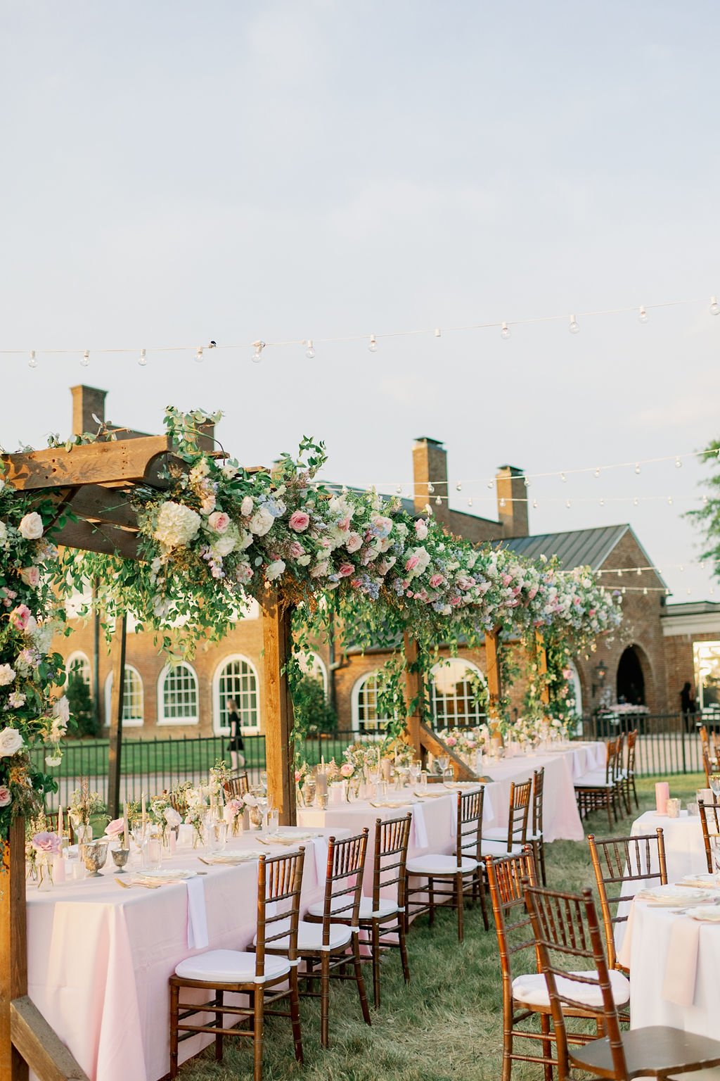 This private estate garden-inspired head table pergola is covered with pink and ivory roses, majolica spray roses, heirloom carnations, blue delphinium, hydrangea and natural greenery. Designed by Rosemary & Finch in Nashville, TN.