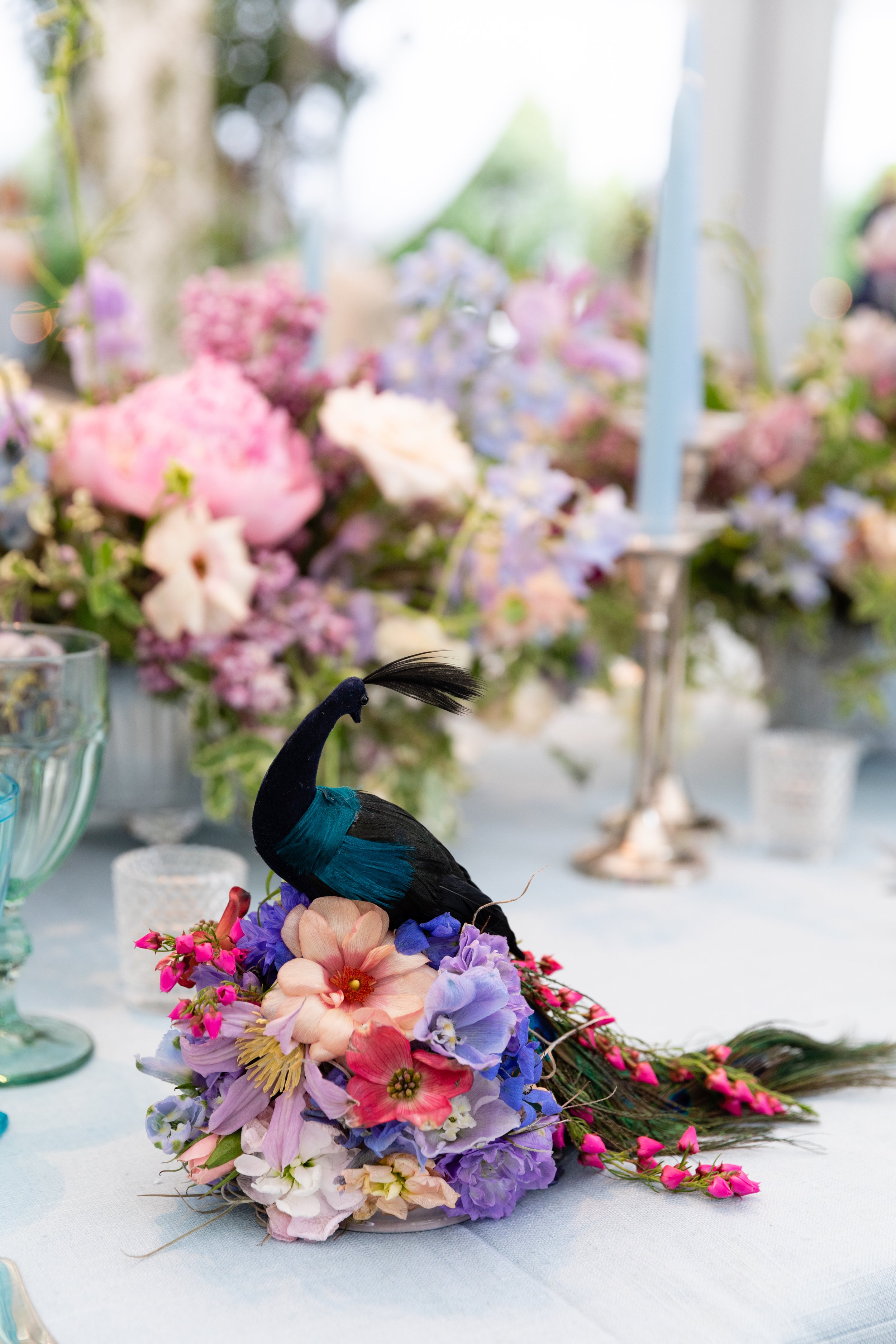 Growing, fresh floral centerpieces with a peacock, including blush garden roses, lilac, blue sweet peas, ranunculus, lavender delphinium, globe allium, and natural greenery for a tented Bridgerton inspired engagement party at a private home in Nashvi