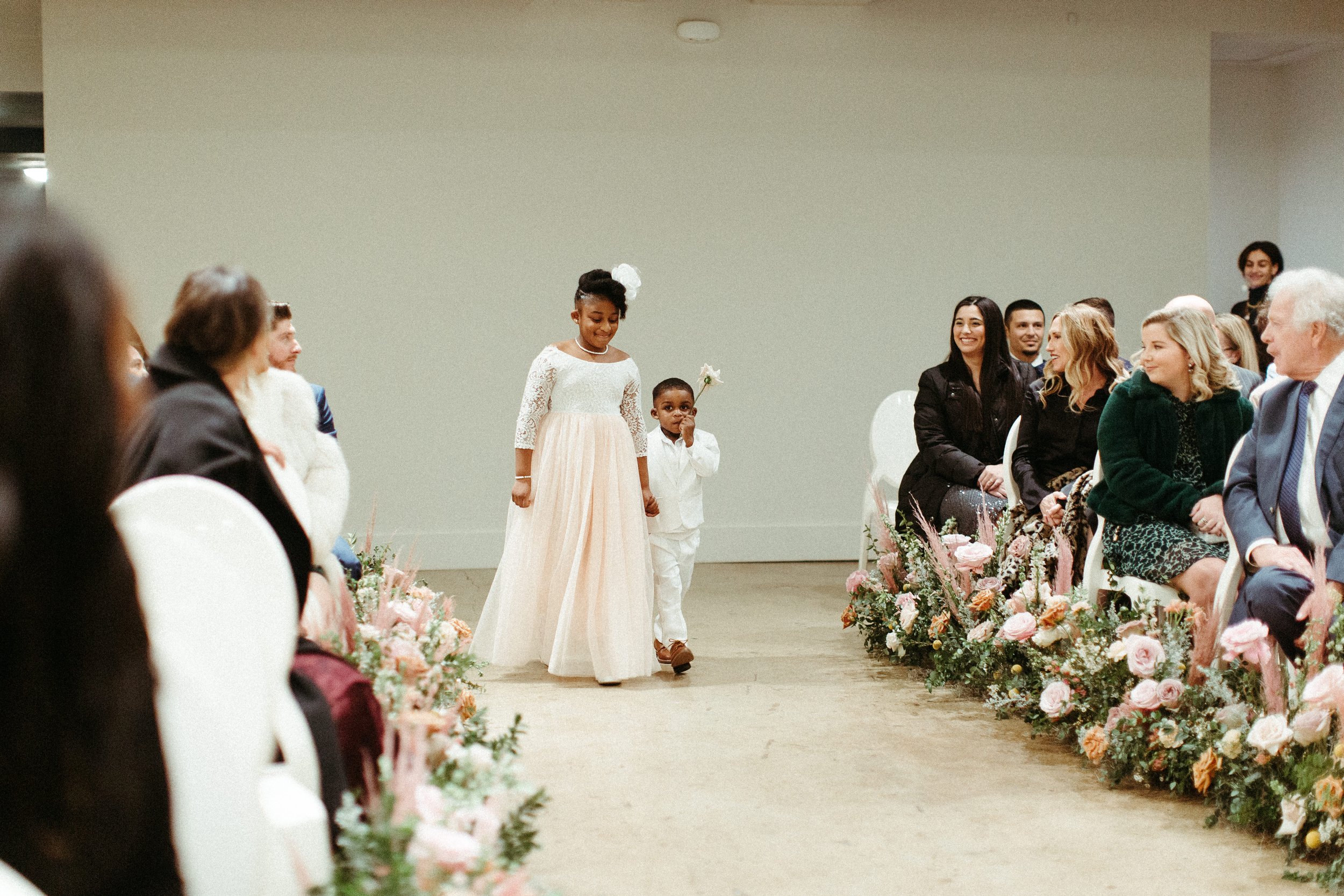 Lush aisle meadows beautifully frame the ceremony of this winter wedding with hues of dusty pink, terra cotta, cream, and sage green. Complete with petal heavy roses and pink pampas grass. Designed by Rosemary and Finch in Nashville, TN.