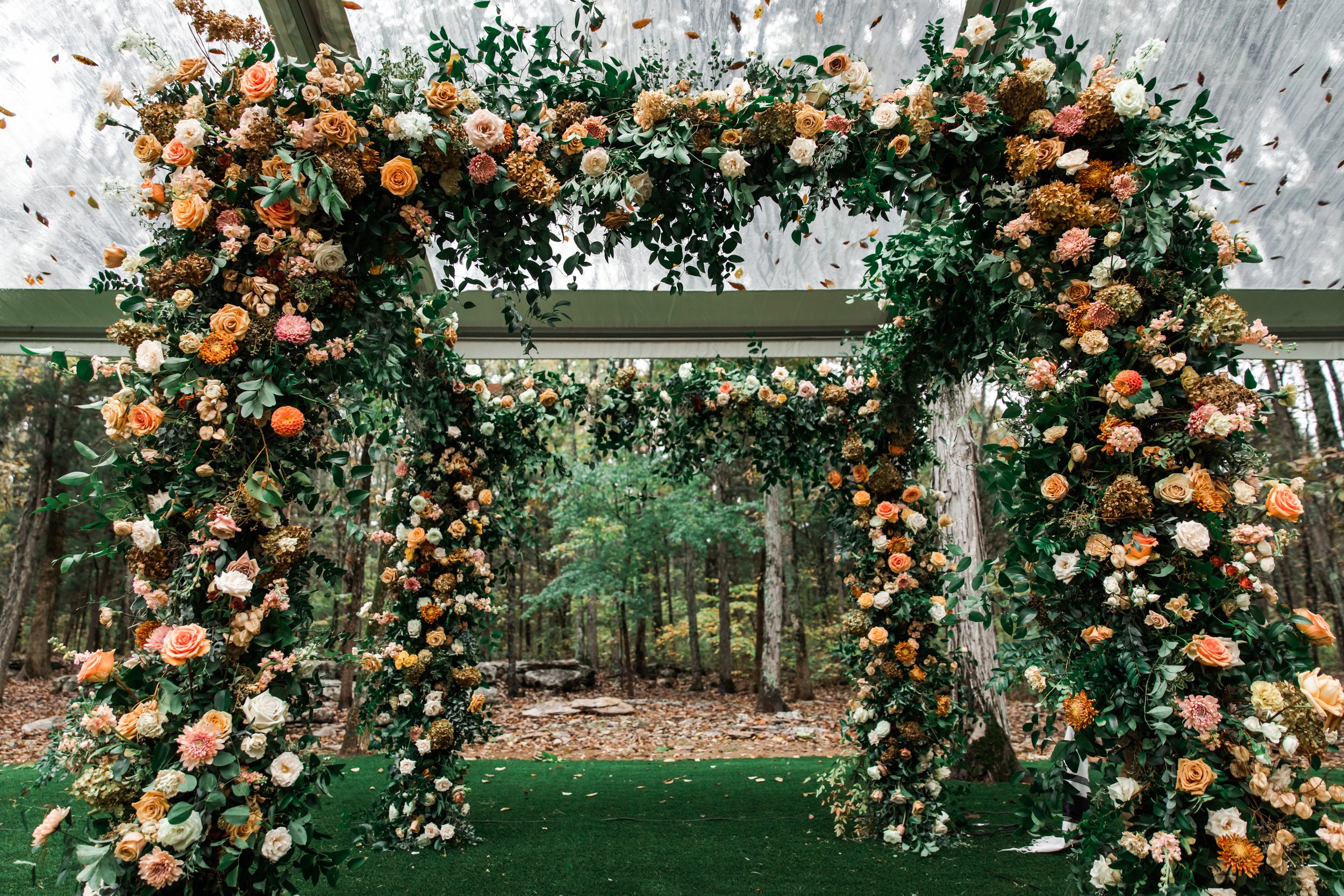 Eye-catching oversized chuppah overflowing with fall florals featuring dahlias, garden roses, rain tree pods, and fall greenery. Autumnal hues of terra cotta, dusty pink, copper, and yellow create this statement wedding piece. Designed by Rosemary an