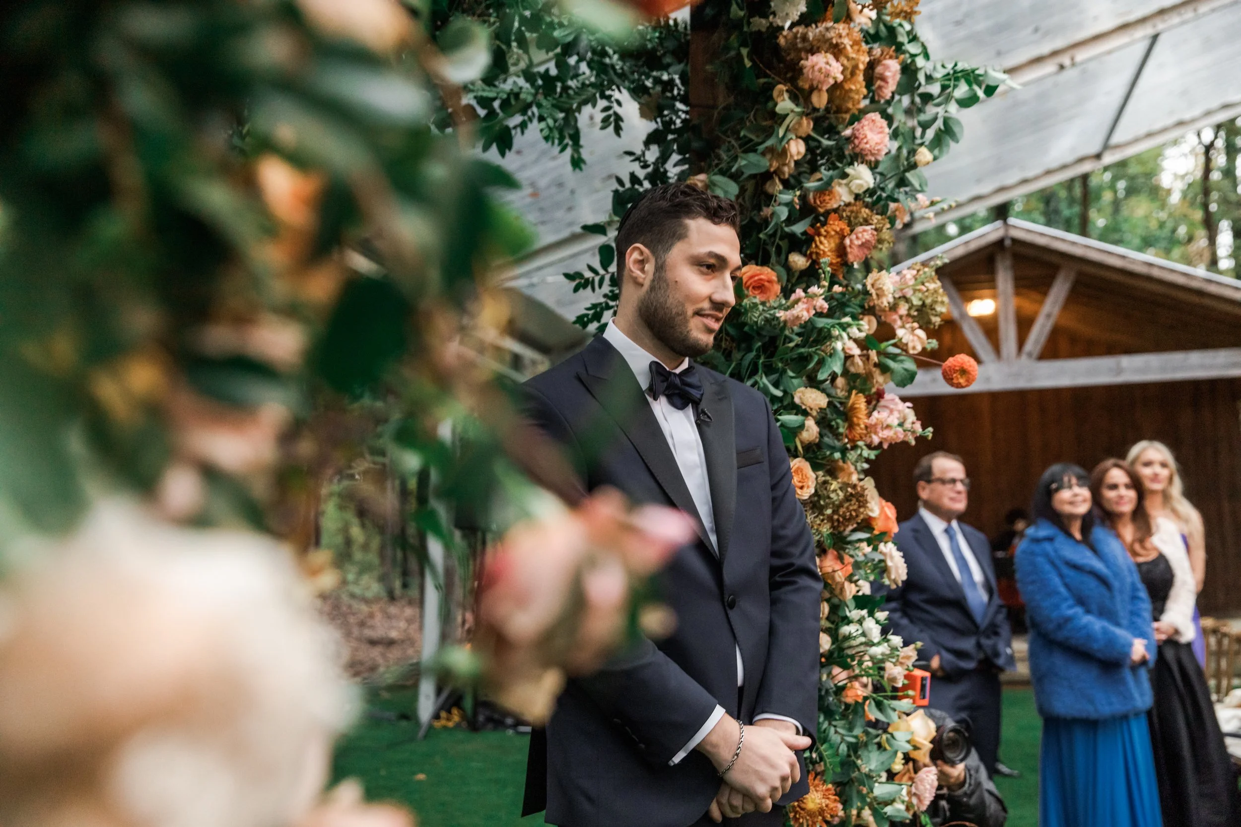 Eye-catching oversized chuppah overflowing with fall florals featuring dahlias, garden roses, rain tree pods, and fall greenery. Autumnal hues of terra cotta, dusty pink, copper, and yellow create this statement wedding piece. Designed by Rosemary an