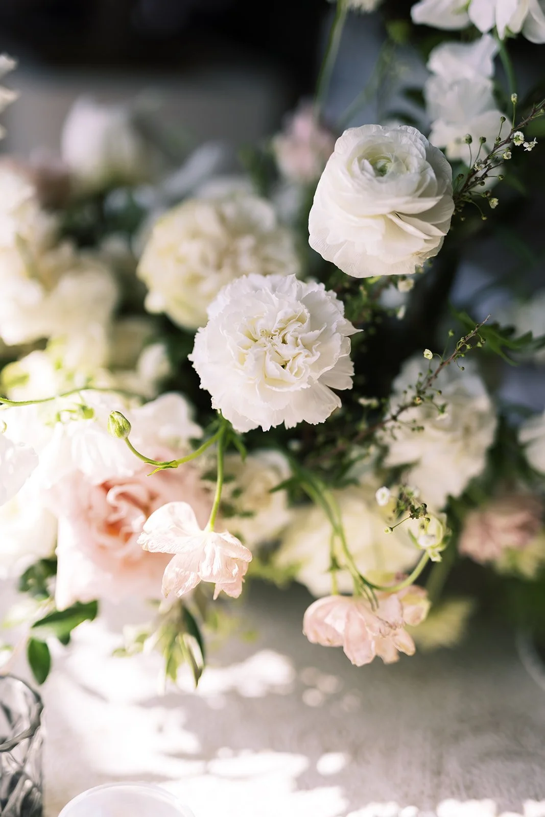 Low floral centerpieces for elegant wedding overflowing with white garden roses, ranunculus, butterfly ranunculus, scabiosa, lisianthus, sweet peas, and natural dark greenery. Floral hues of white, cream, and blush. Designed by Rosemary and Finch in