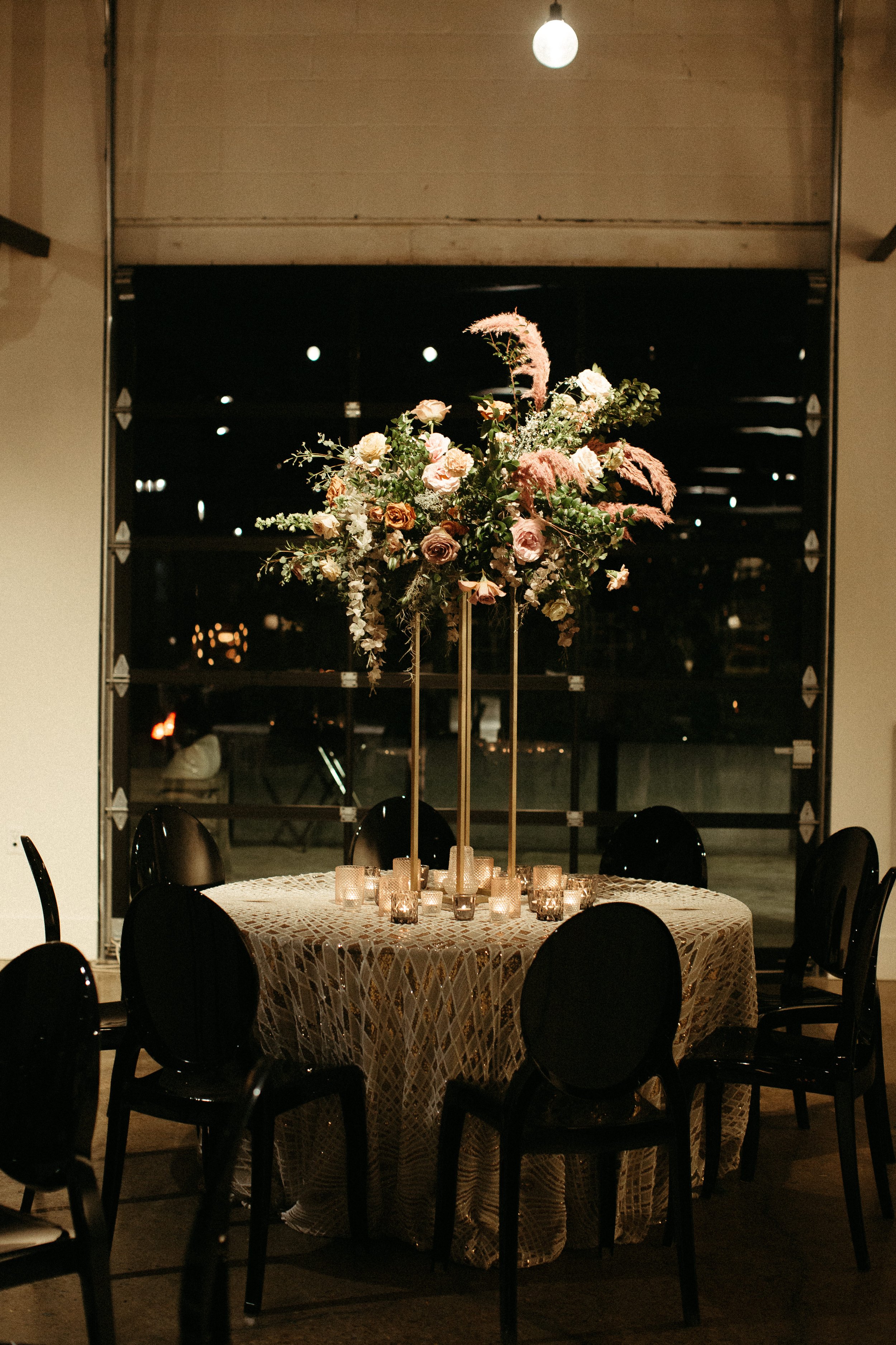 Stunning elevated centerpieces decorate this art deco wedding. Floral hues of terra cotta, mauve, burgundy, and dusty pink are brought to life with petal heavy roses, dried branches, and pink pampas grass. Designed by Rosemary and Finch in Nashville,