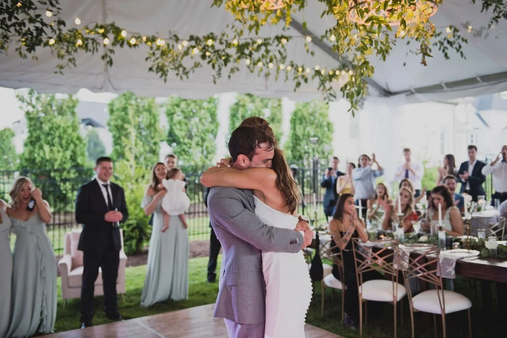 This backyard reception had a lush head table filled with garlands of eucalyptus, garden roses, ruscus, and spray roses. Smilax covers the chandelier and string lights. Designed by Rosemary and Finch in Nashville, TN.