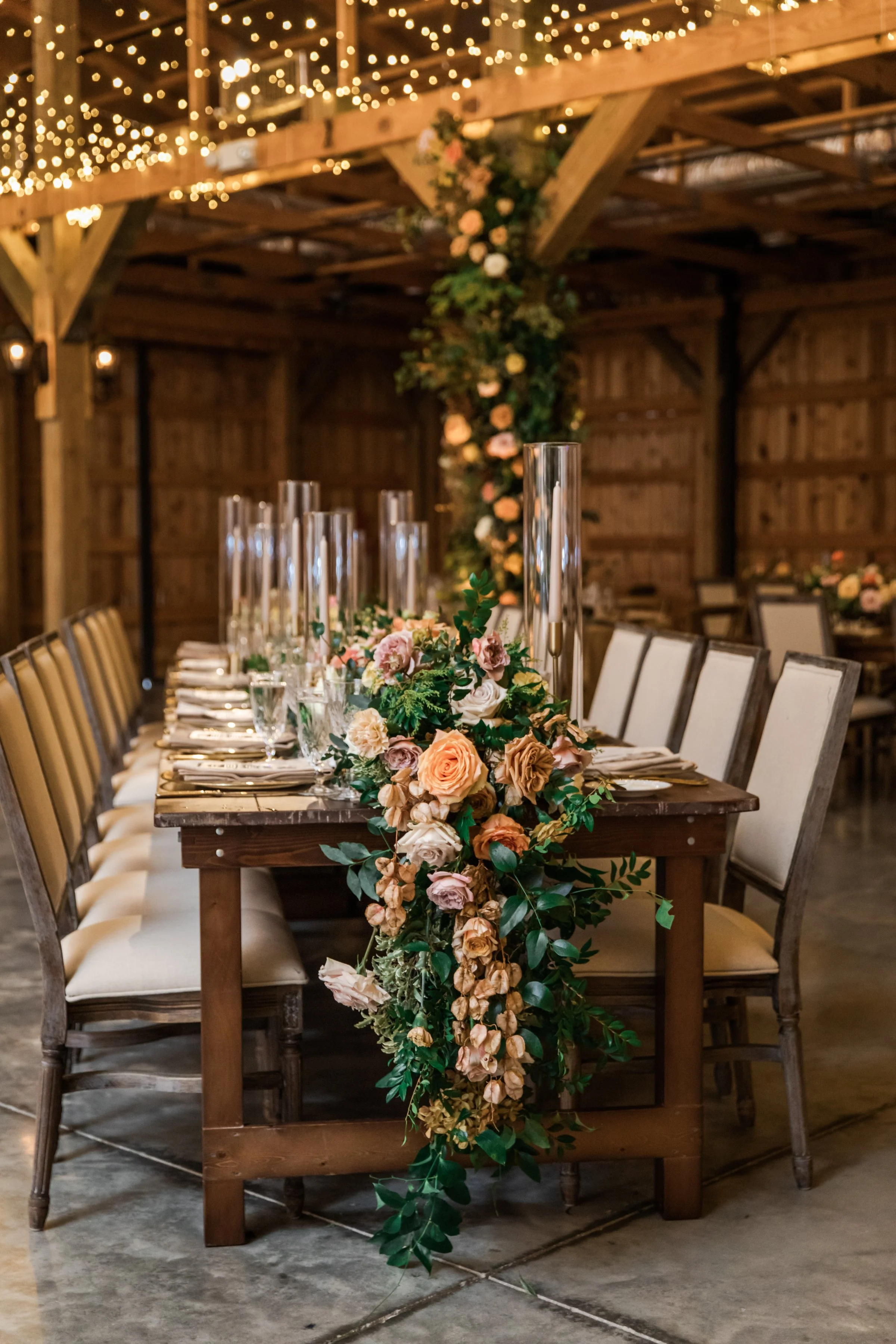 Stunning floral cascades line tables of this fall reception with terra cotta, blush, yellow hues, and taupe taper candles. Florals featuring dahlias, roses, and rain tree pods create lush arrangements. Designed by Rosemary and Finch in Nashville, TN.