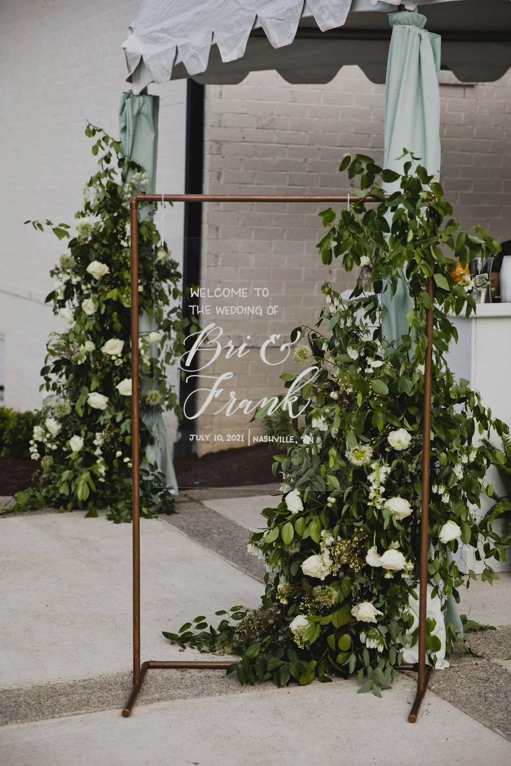 A welcome sign installation dripping in white garden roses, delphinium, spray roses, and sprawling smilax. Designed by Rosemary and Finch in Nashville, TN.