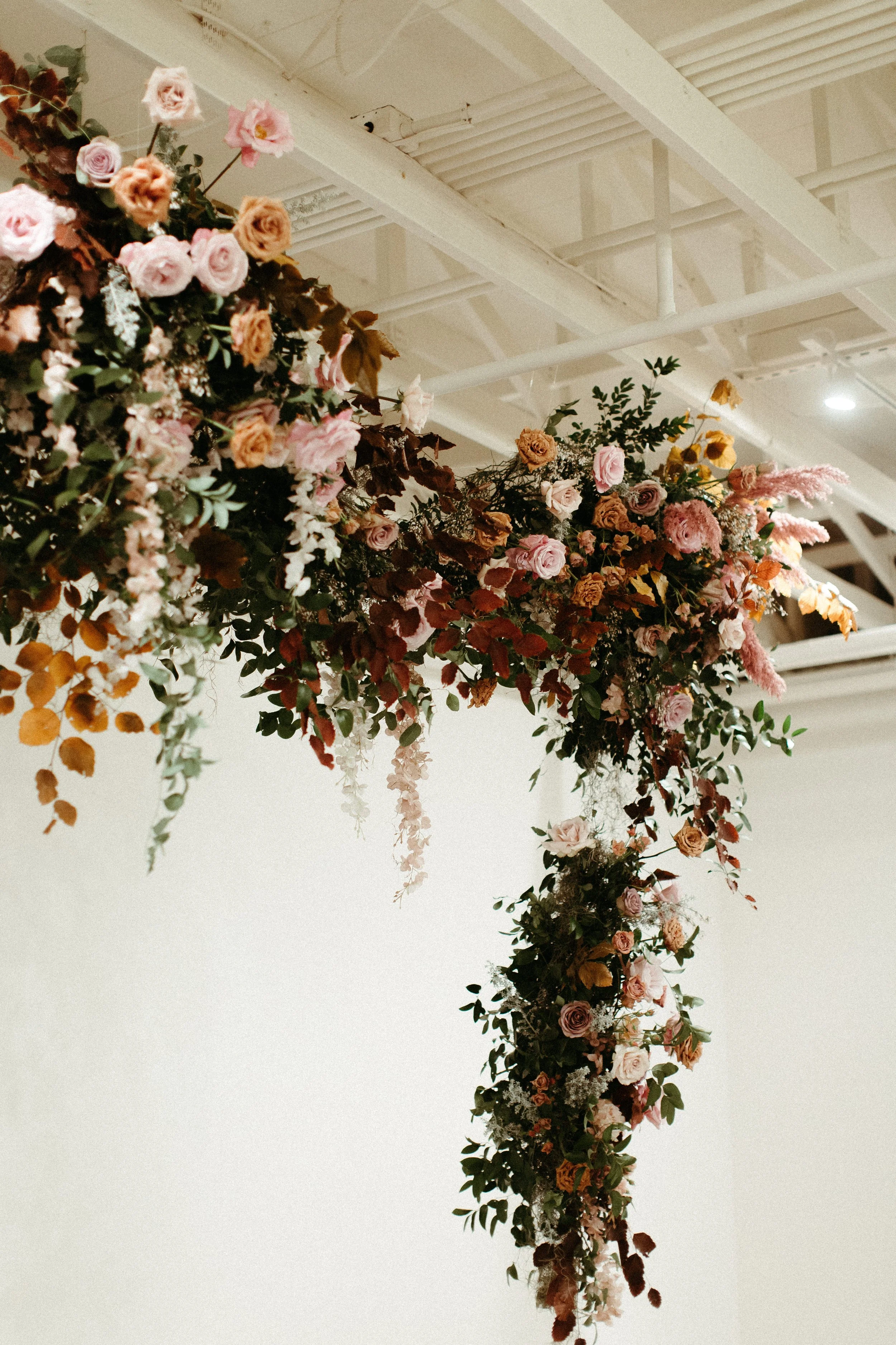 An eye-catching whimsical installation full of petal heavy roses and copper beech was the highlight of this art deco wedding. Terra cotta, burgundy, dusty pink, and other neutral florals warm up this ceremony. Designed by Rosemary and Finch in Nashvi