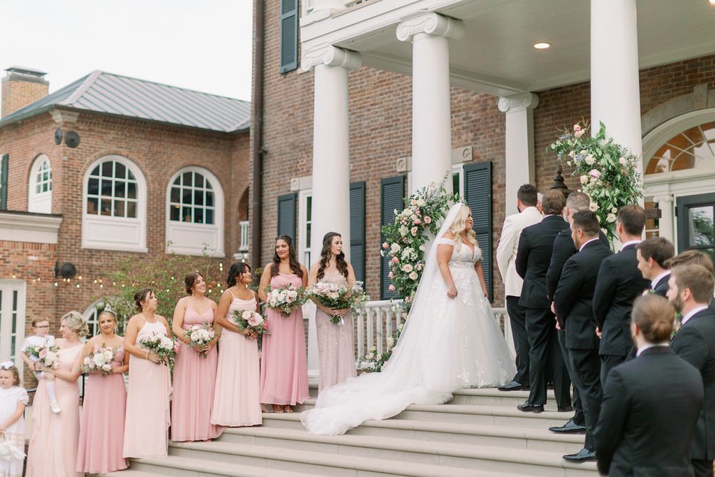 An organic growing arch filled with blush and ivory roses, majolica spray roses, champagne roses, hydrangea, and lush sprawling greenery and accented with low growing aisle markers. Designed by Rosemary & Finch in Nashville, TN.