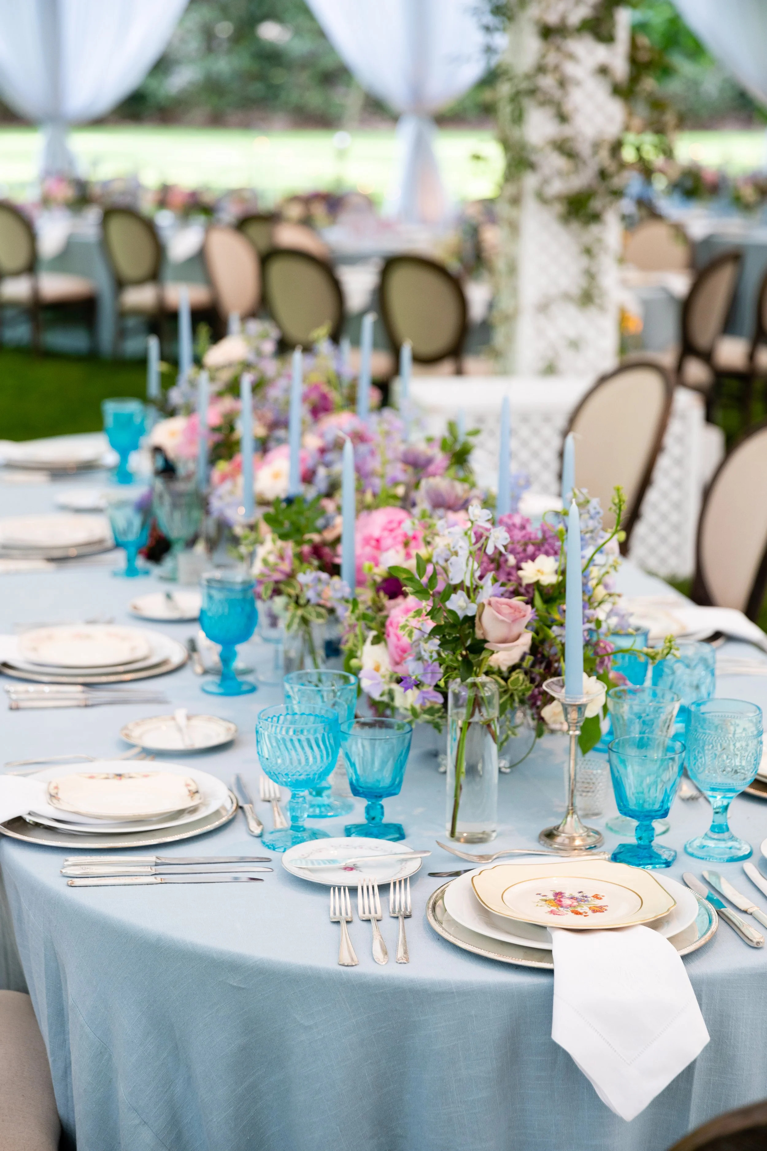 Growing, fresh floral centerpieces with blush garden roses, lilac, blue sweet peas, ranunculus, lavender delphinium, globe allium, clematis, and natural greenery for a tented Bridgerton inspired engagement party at a private home in Nashville, TN. Fl
