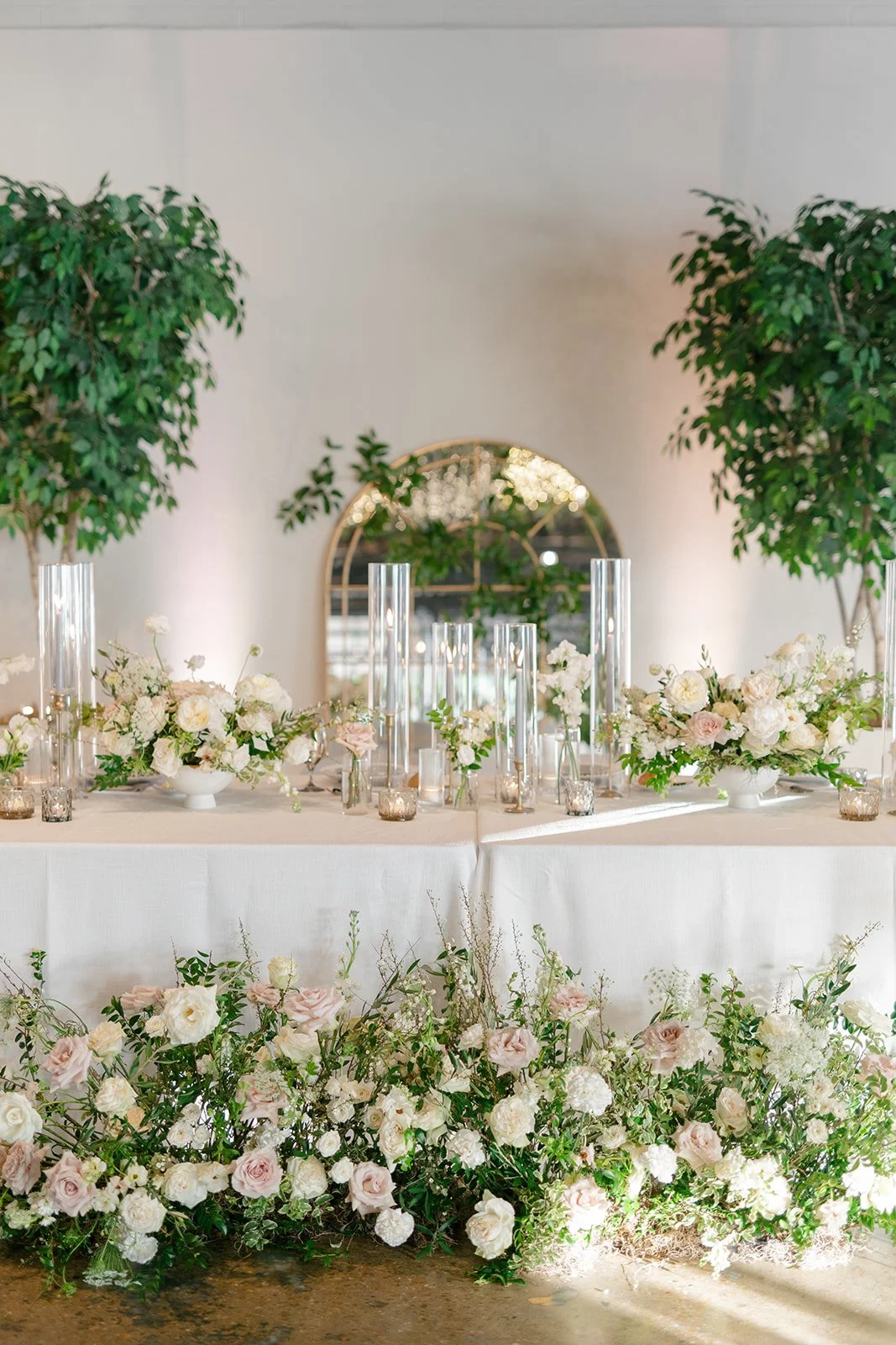 Low floral centerpieces for elegant wedding overflowing with white garden roses, ranunculus, butterfly ranunculus, scabiosa, lisianthus, sweet peas, and natural dark greenery. Floral hues of white, cream, and blush. Designed by Rosemary and Finch in
