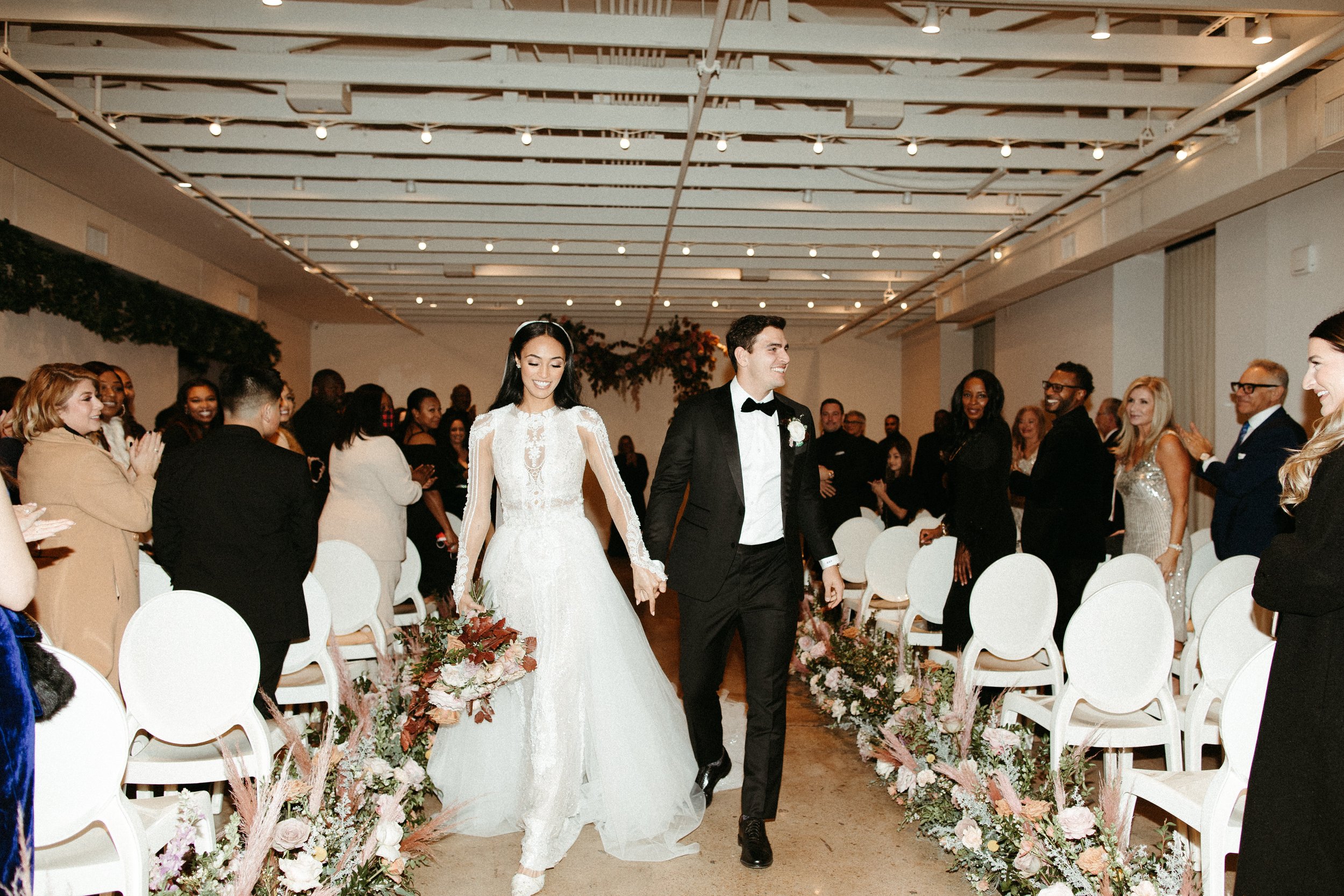 Lush aisle meadows beautifully frame the ceremony of this winter wedding with hues of dusty pink, terra cotta, cream, and sage green. Complete with petal heavy roses and pink pampas grass. Designed by Rosemary and Finch in Nashville, TN.