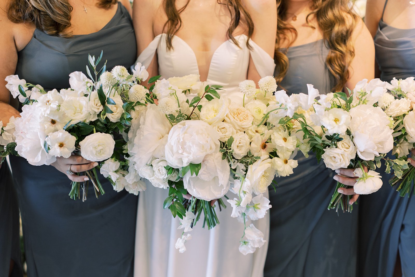 Bridal party florals of white garden roses, peonies, ranunculus, sweet peas, scabiosa, butterfly ranunculus and dark greenery in floral hues of white, cream, and blush. Designed by Rosemary and Finch in Nashville, TN.