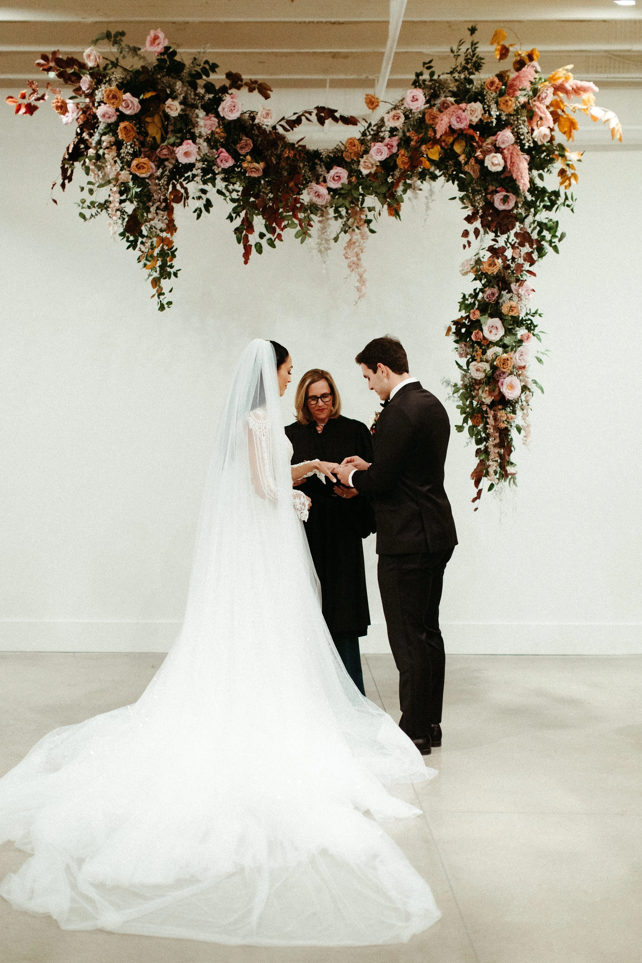 An eye-catching whimsical installation full of petal heavy roses and copper beech was the highlight of this art deco wedding. Terra cotta, burgundy, dusty pink, and other neutral florals warm up this ceremony. Designed by Rosemary and Finch in Nashvi