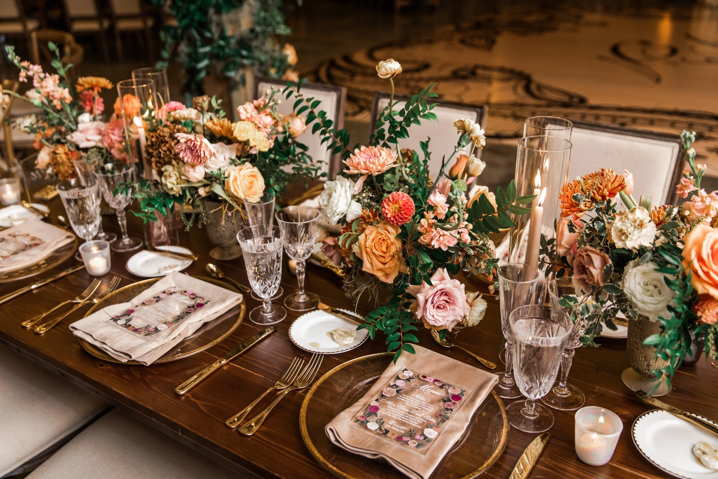Beautiful fall floral centerpieces warm this reception space with a sunset color palette. Garden roses, ranunculus, double brownie tulips, and lisianthus create hues of terra cotta, blush pink, copper, and yellow. Designed by Rosemary and Finch in Na