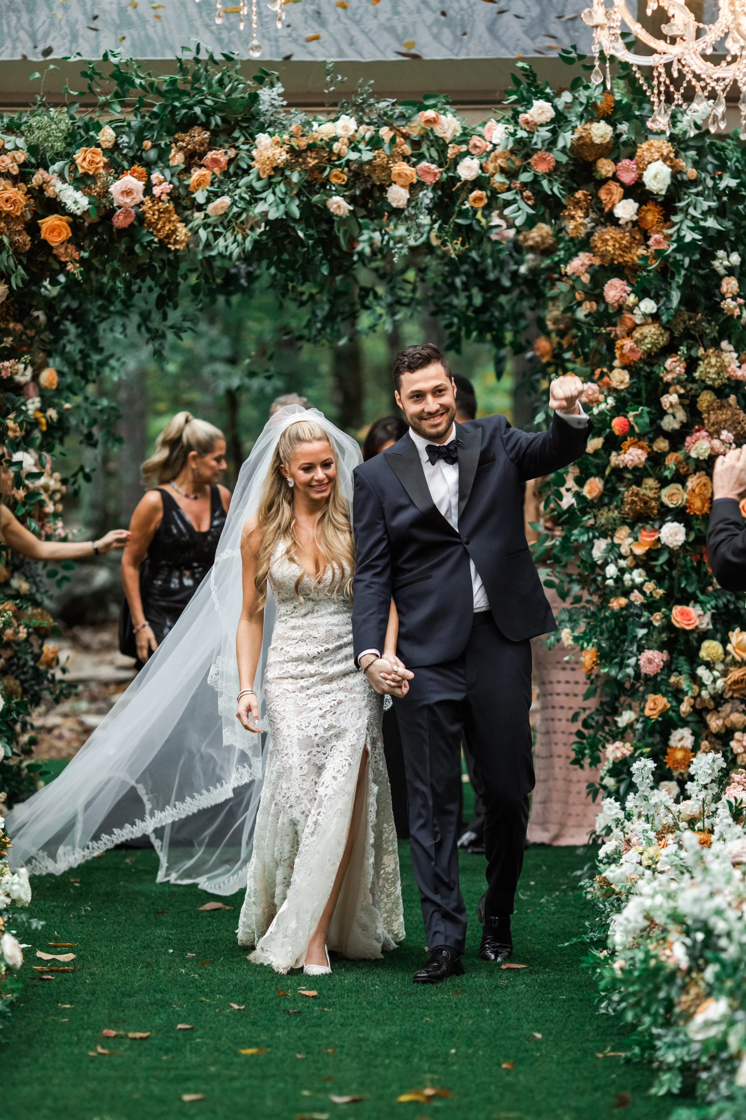 Eye-catching oversized chuppah overflowing with fall florals featuring dahlias, garden roses, rain tree pods, and fall greenery. Autumnal hues of terra cotta, dusty pink, copper, and yellow create this statement wedding piece. Designed by Rosemary an