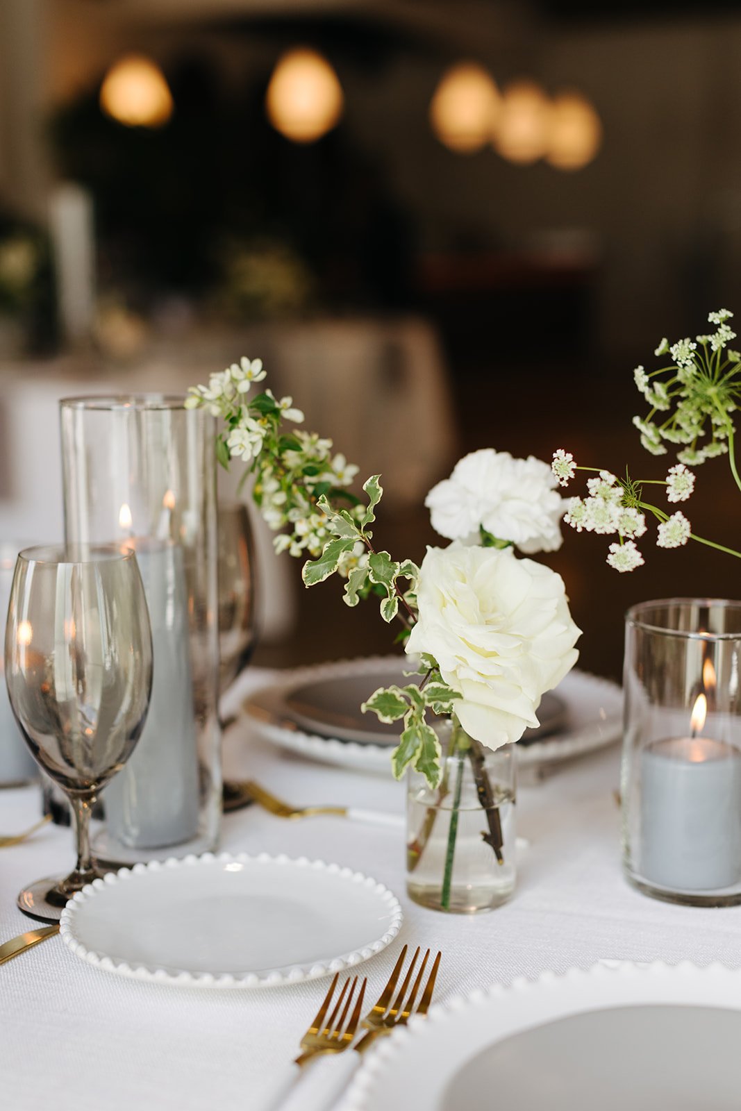 Elegant bud vases with florals of roses, ranunculus, sweet peas, Queen Anne’s lace, butterfly ranunculus in hues of white, cream and blush. Accented with dusty blue tapers and clear glass votives. Designed by Rosemary and Finch in Nashville, TN.