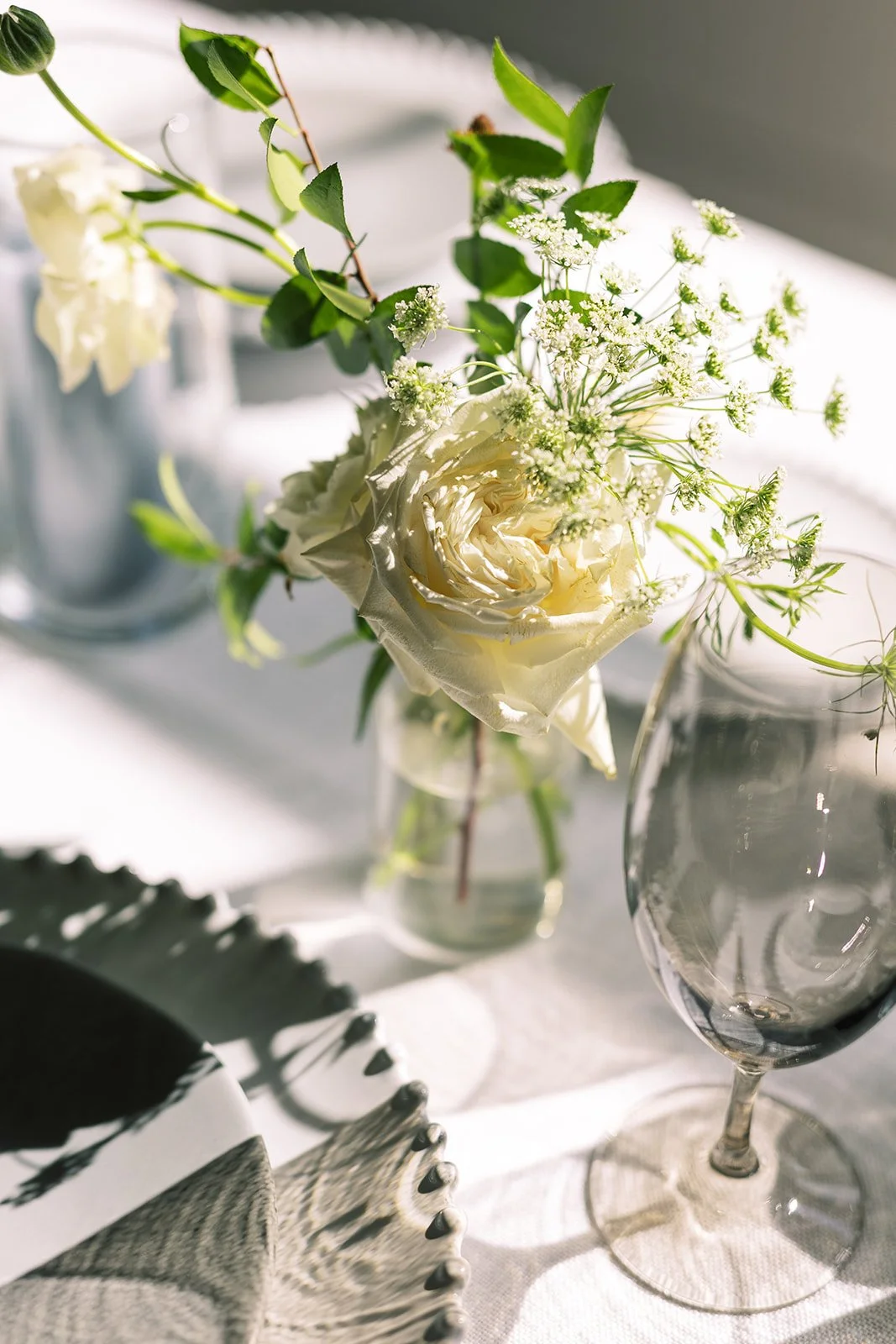 Elegant bud vases with florals of roses, ranunculus, sweet peas, Queen Anne’s lace, butterfly ranunculus in hues of white, cream and blush. Accented with dusty blue tapers and clear glass votives. Designed by Rosemary and Finch in Nashville, TN.