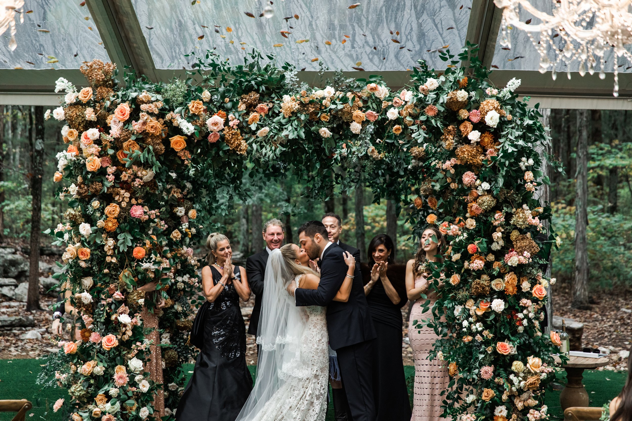 Eye-catching oversized chuppah overflowing with fall florals featuring dahlias, garden roses, rain tree pods, and fall greenery. Autumnal hues of terra cotta, dusty pink, copper, and yellow create this statement wedding piece. Designed by Rosemary an