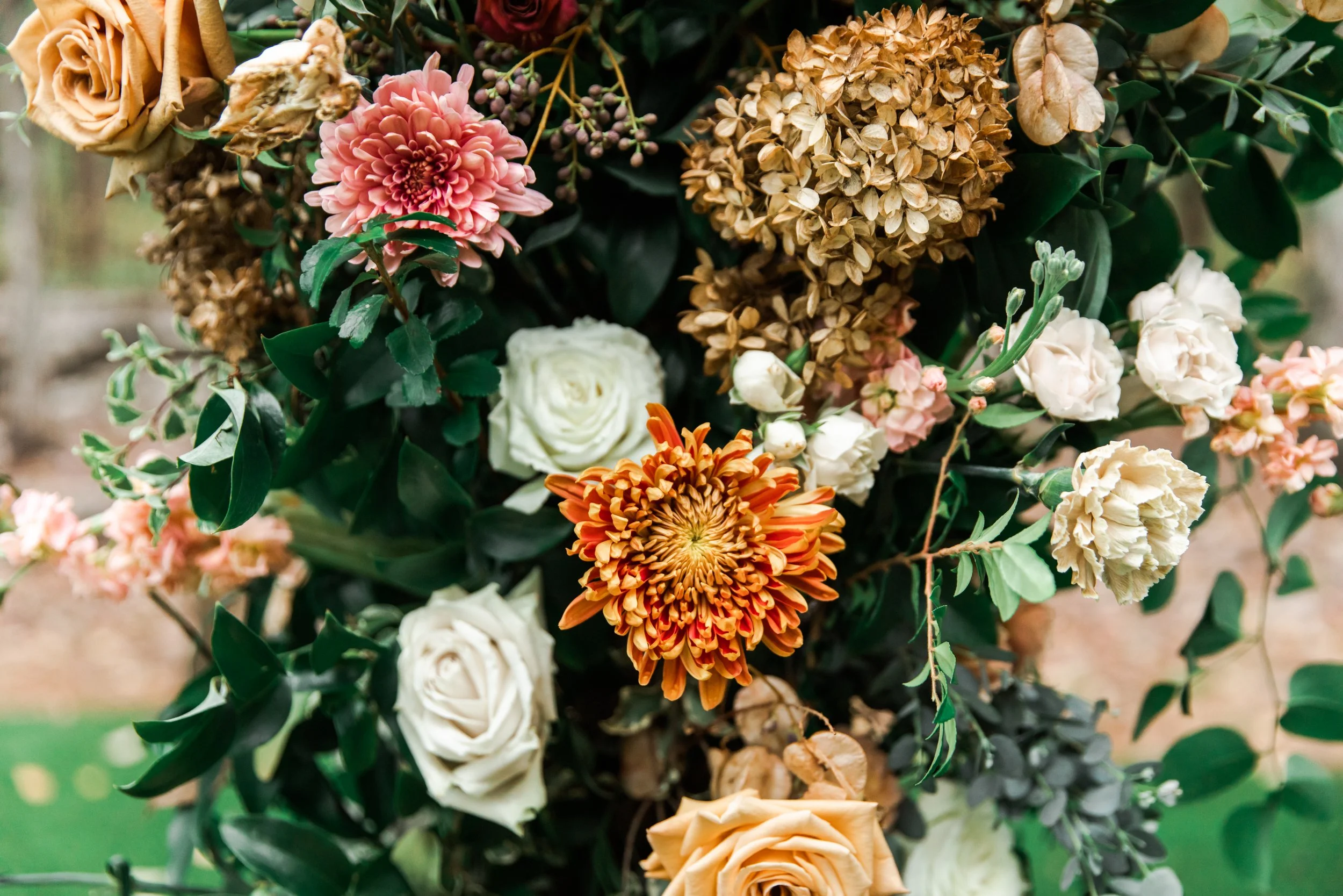 Eye-catching oversized chuppah overflowing with fall florals featuring dahlias, garden roses, rain tree pods, and fall greenery. Autumnal hues of terra cotta, dusty pink, copper, and yellow create this statement wedding piece. Designed by Rosemary an