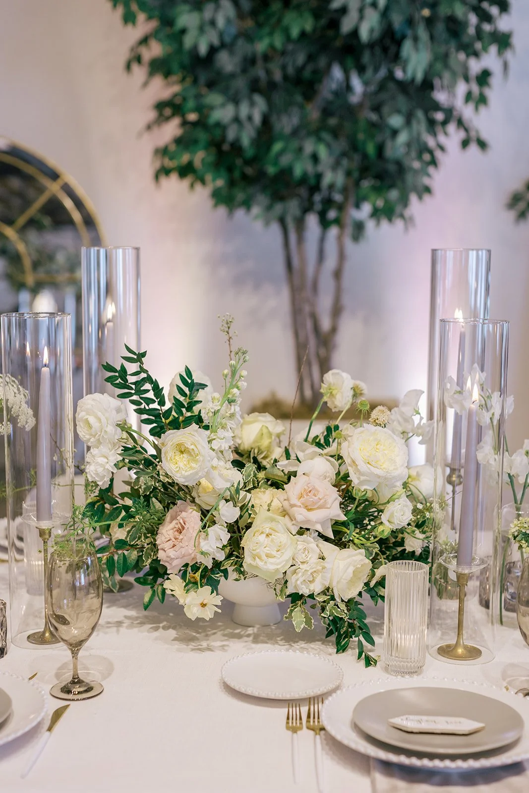 Low floral centerpieces for elegant wedding overflowing with white garden roses, ranunculus, butterfly ranunculus, scabiosa, lisianthus, sweet peas, and natural dark greenery. Floral hues of white, cream, and blush. Designed by Rosemary and Finch in