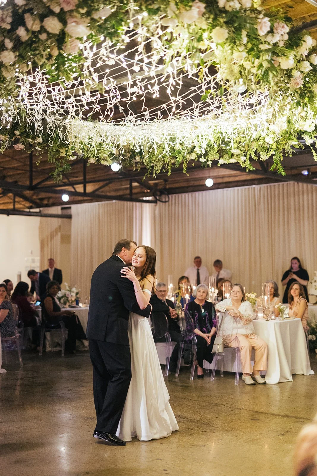 Lush floral chandelier lights up the dance floor with florals of petal heavy roses, ranunculus, lisianthus, delphinium, and dark greenery in hues of white, cream, and blush. Designed by Rosemary and Finch in Nashville, TN.