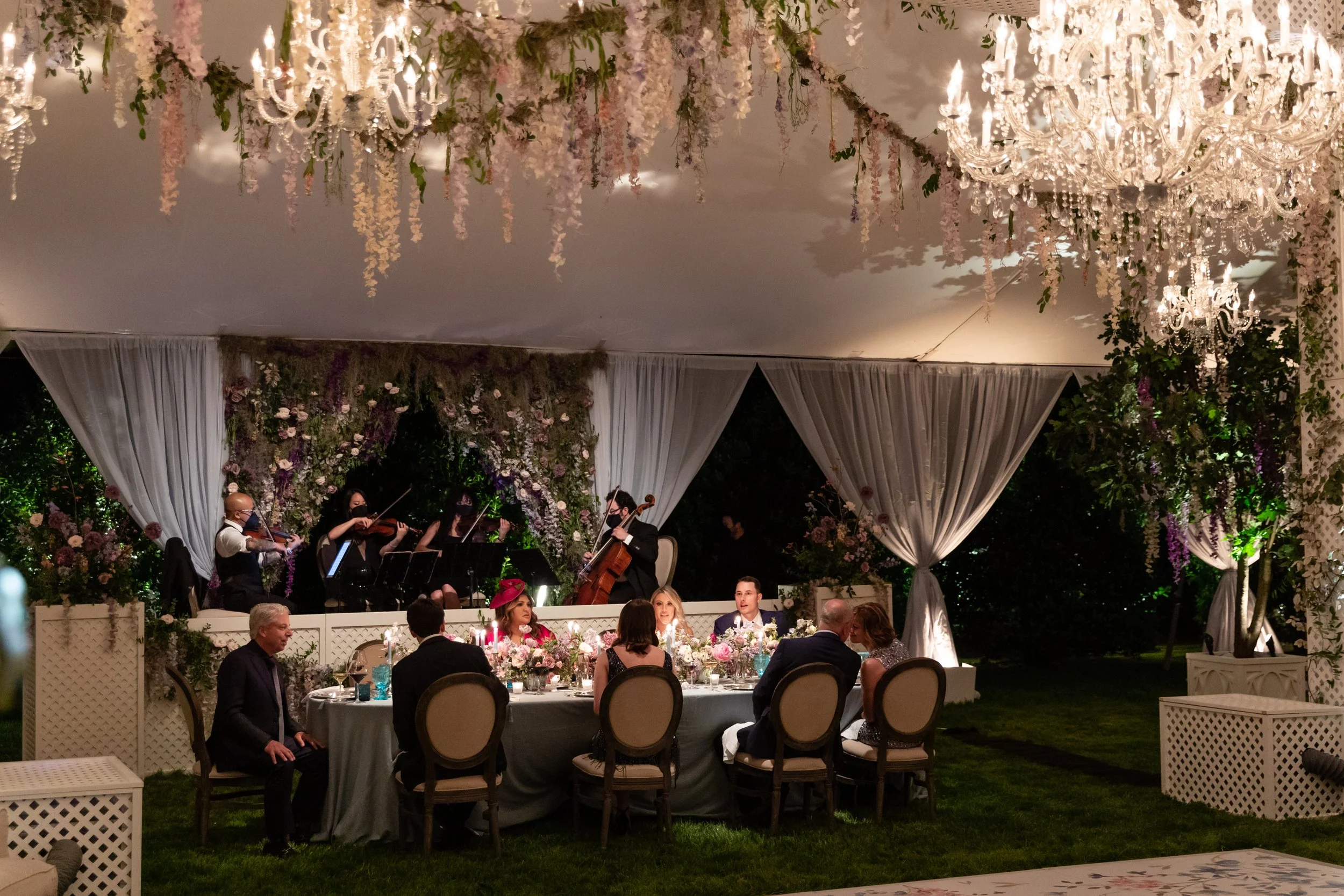 Growing, fresh floral installations and chandeliers with blush garden roses, lavender delphinium, wisteria, globe allium, and vines and greenery for a tented Bridgerton inspired engagement party at a private home in Nashville, TN.