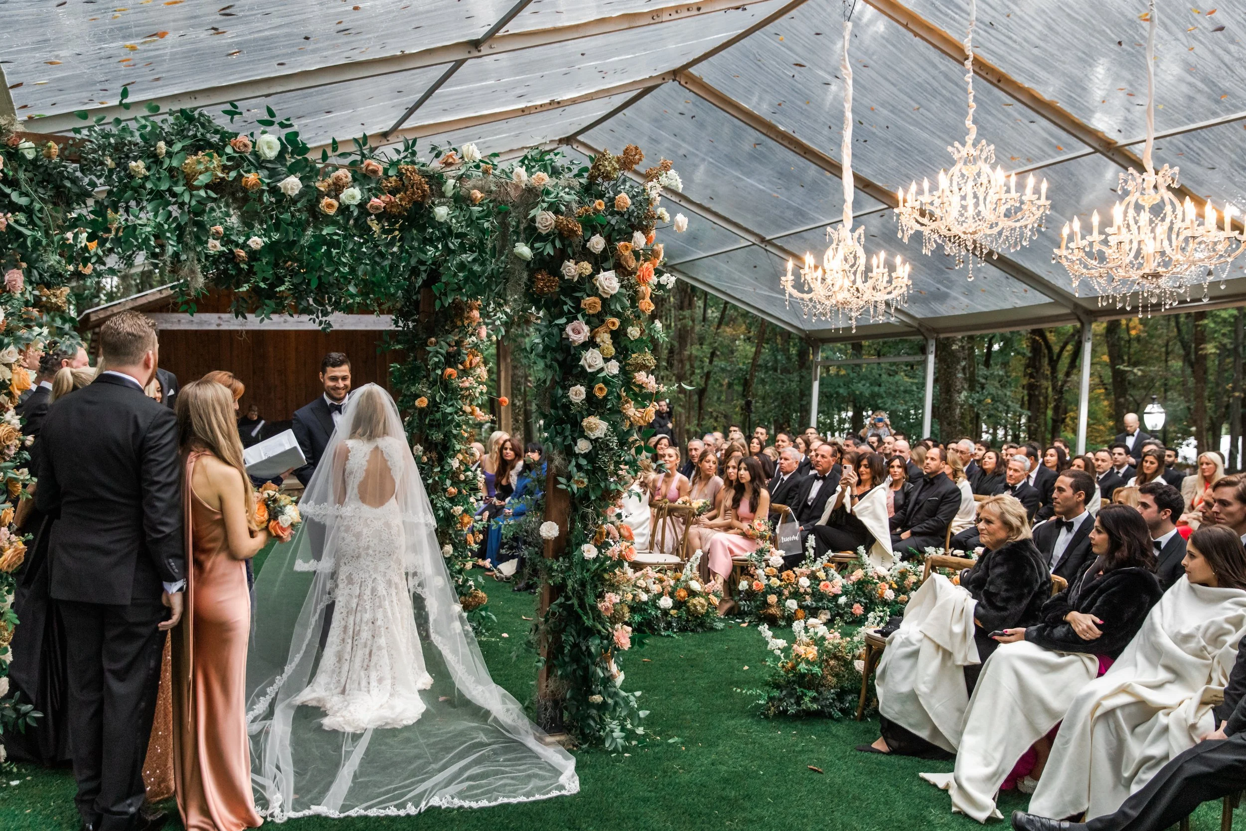 Eye-catching oversized chuppah overflowing with fall florals featuring dahlias, garden roses, rain tree pods, and fall greenery. Autumnal hues of terra cotta, dusty pink, copper, and yellow create this statement wedding piece. Designed by Rosemary an