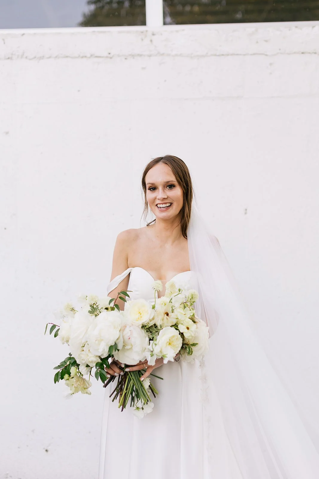 Bridal bouquet of white garden roses, peonies, ranunculus, sweet peas, scabiosa, butterfly ranunculus and dark greenery in floral hues of white, cream, and blush. Designed by Rosemary and Finch in Nashville, TN.