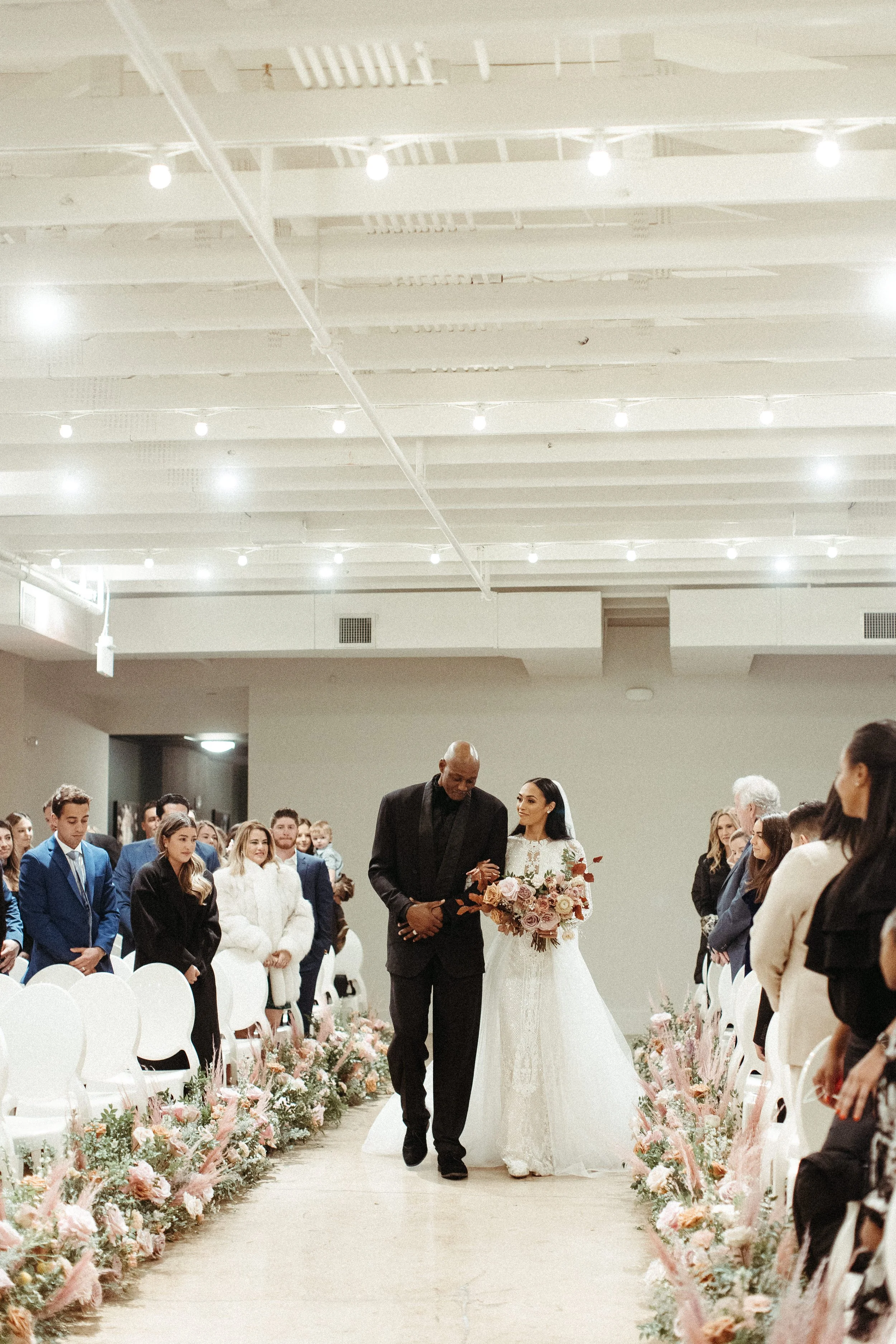 Lush aisle meadows beautifully frame the ceremony of this winter wedding with hues of dusty pink, terra cotta, cream, and sage green. Complete with petal heavy roses and pink pampas grass. Designed by Rosemary and Finch in Nashville, TN.