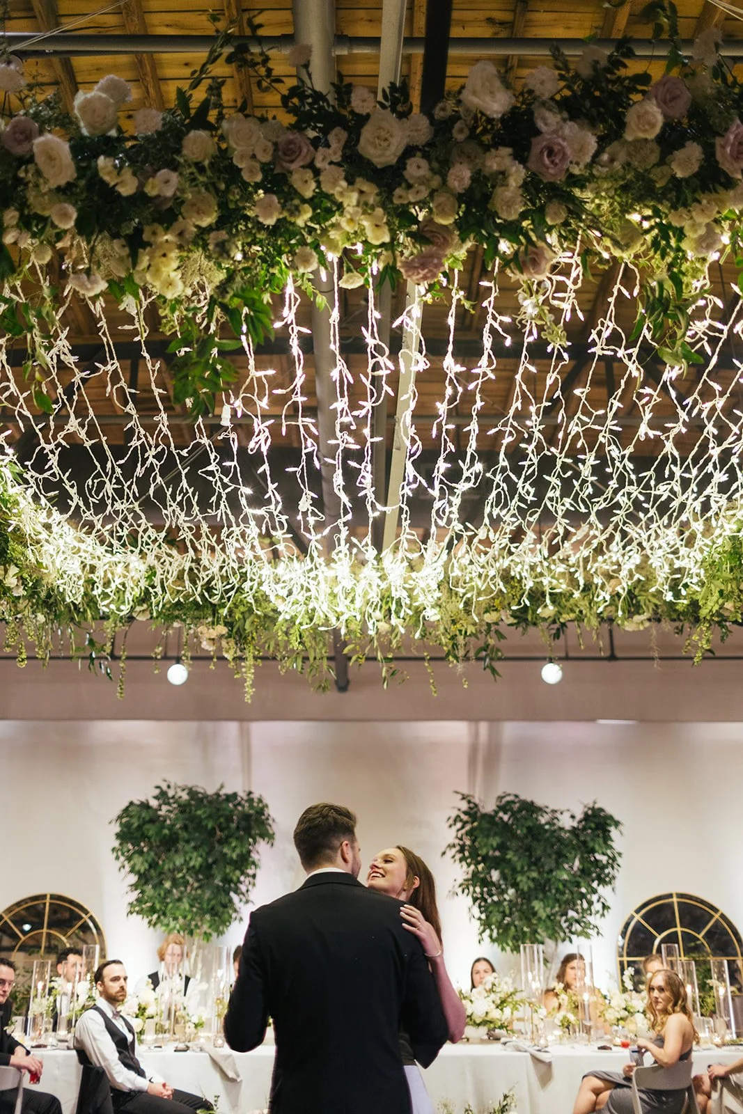 Lush floral chandelier lights up the dance floor with florals of petal heavy roses, ranunculus, lisianthus, delphinium, and dark greenery in hues of white, cream, and blush. Designed by Rosemary and Finch in Nashville, TN.