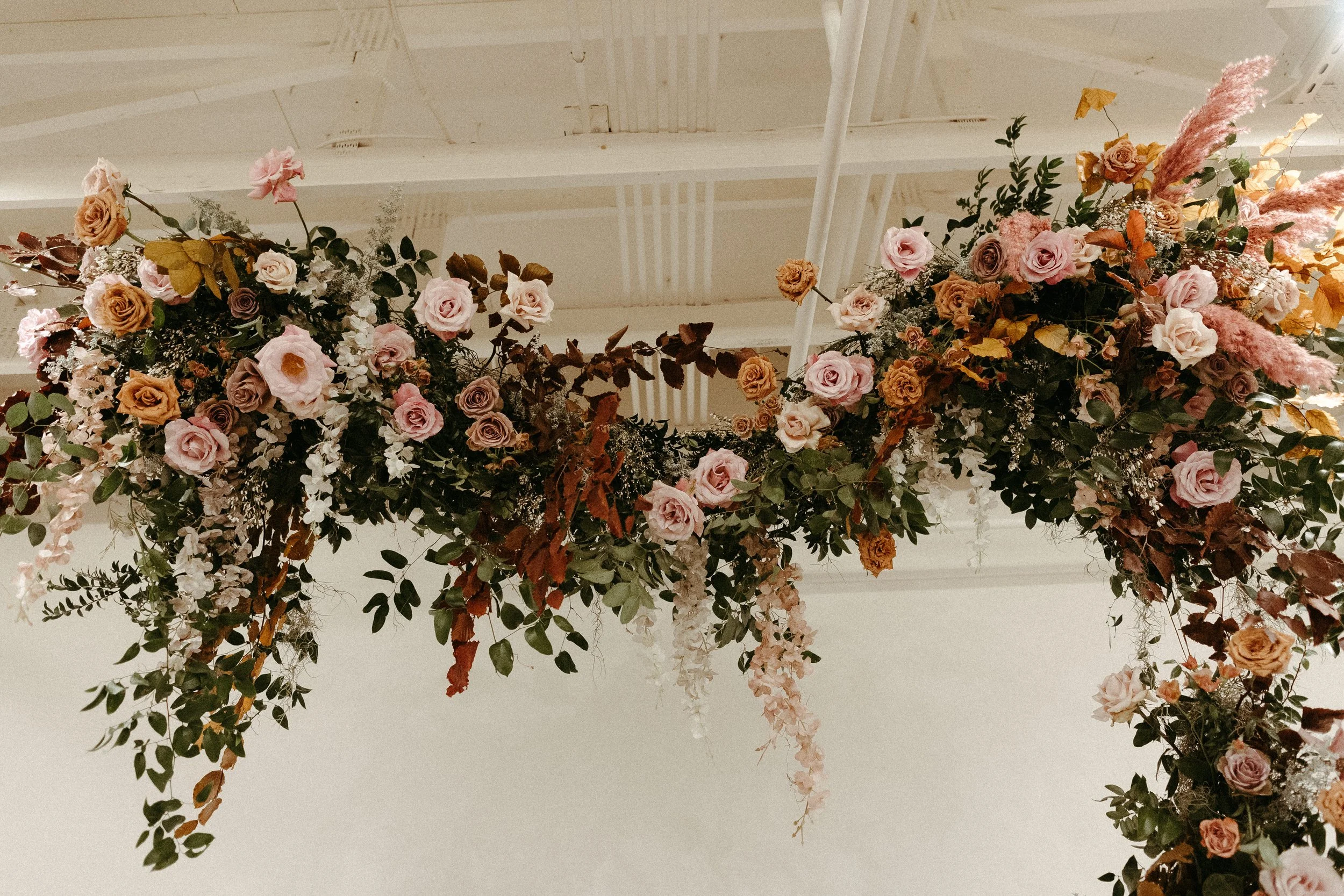 An eye-catching whimsical installation full of petal heavy roses and copper beech was the highlight of this art deco wedding. Terra cotta, burgundy, dusty pink, and other neutral florals warm up this ceremony. Designed by Rosemary and Finch in Nashvi