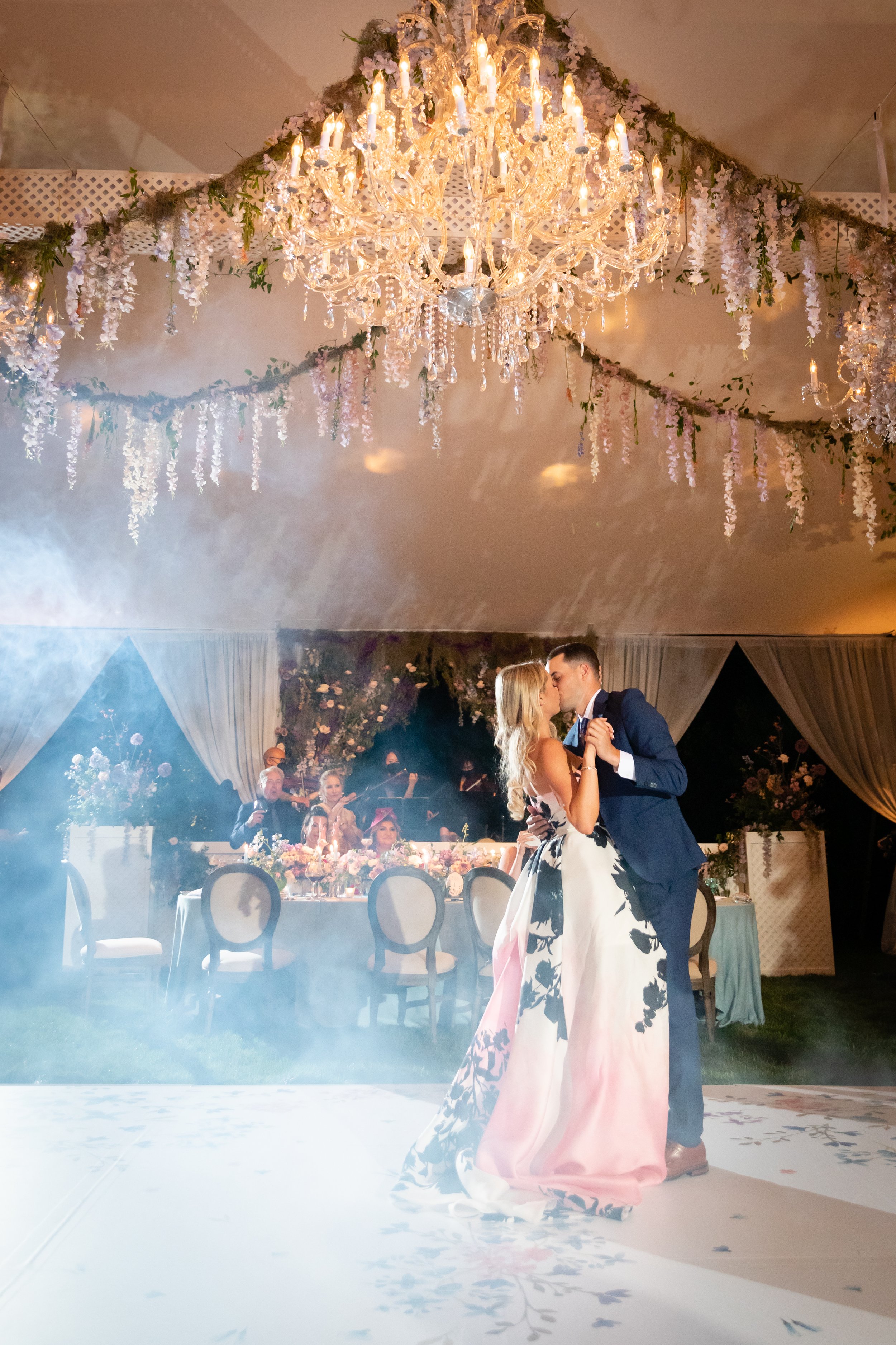 Growing, fresh floral installations and chandeliers with blush garden roses, lavender delphinium, wisteria, globe allium, and vines and greenery for a tented Bridgerton inspired engagement party at a private home in Nashville, TN.