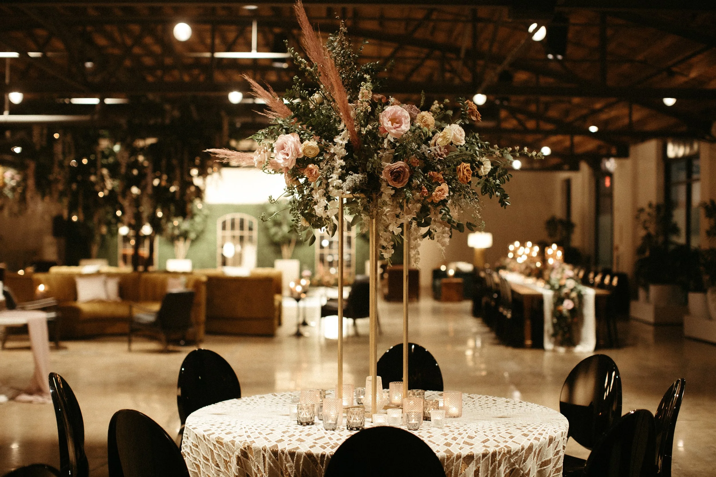 Stunning elevated centerpieces decorate this art deco wedding. Floral hues of terra cotta, mauve, burgundy, and dusty pink are brought to life with petal heavy roses, dried branches, and pink pampas grass. Designed by Rosemary and Finch in Nashville,
