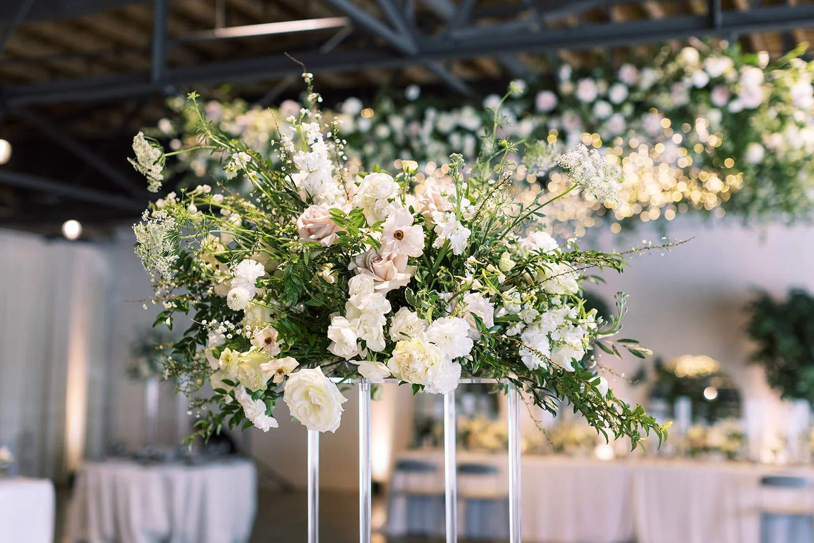 Elevated lucite stands with lush floral centerpieces of white garden roses, ranunculus, delphinium, lisianthus, Queen Anne’s lace and natural, untamed greenery. Floral hues of white, cream, and blush. Designed by Rosemary and Finch in Nashville, TN.