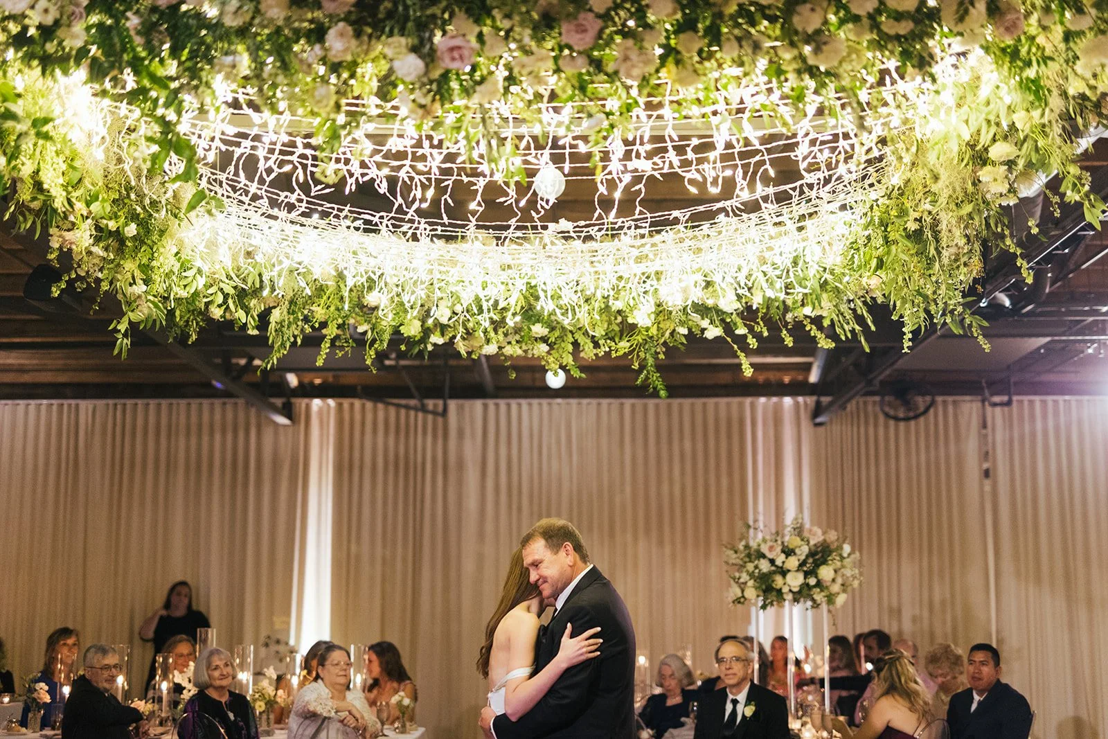 Lush floral chandelier lights up the dance floor with florals of petal heavy roses, ranunculus, lisianthus, delphinium, and dark greenery in hues of white, cream, and blush. Designed by Rosemary and Finch in Nashville, TN.