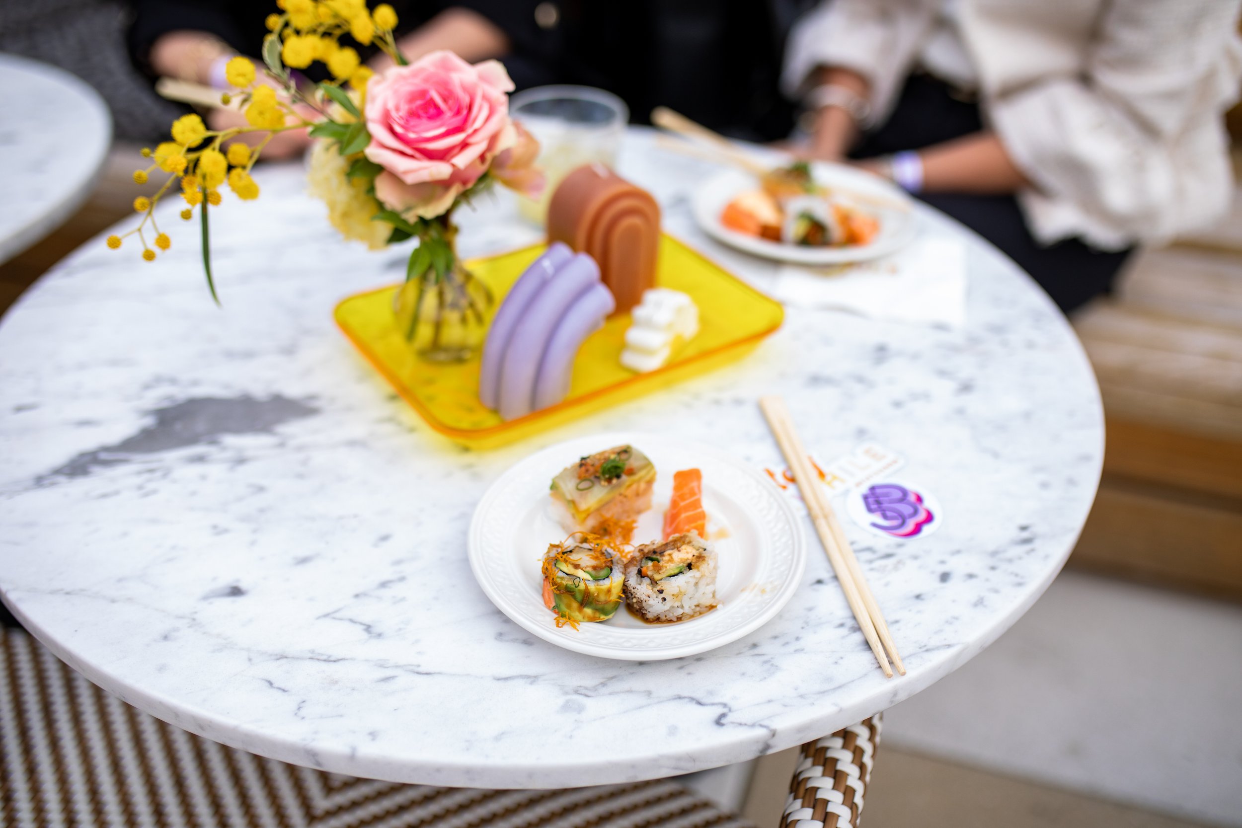 Dainty bud vases composed of roses, sweet peas, and ranunculus in floral hues of rich magenta, lavender, dusty pink, yellow, and mixed greenery. Paired with candles of unique shapes and hues. Design for Fifth + Broadway Spring by Rosemary and Finch.