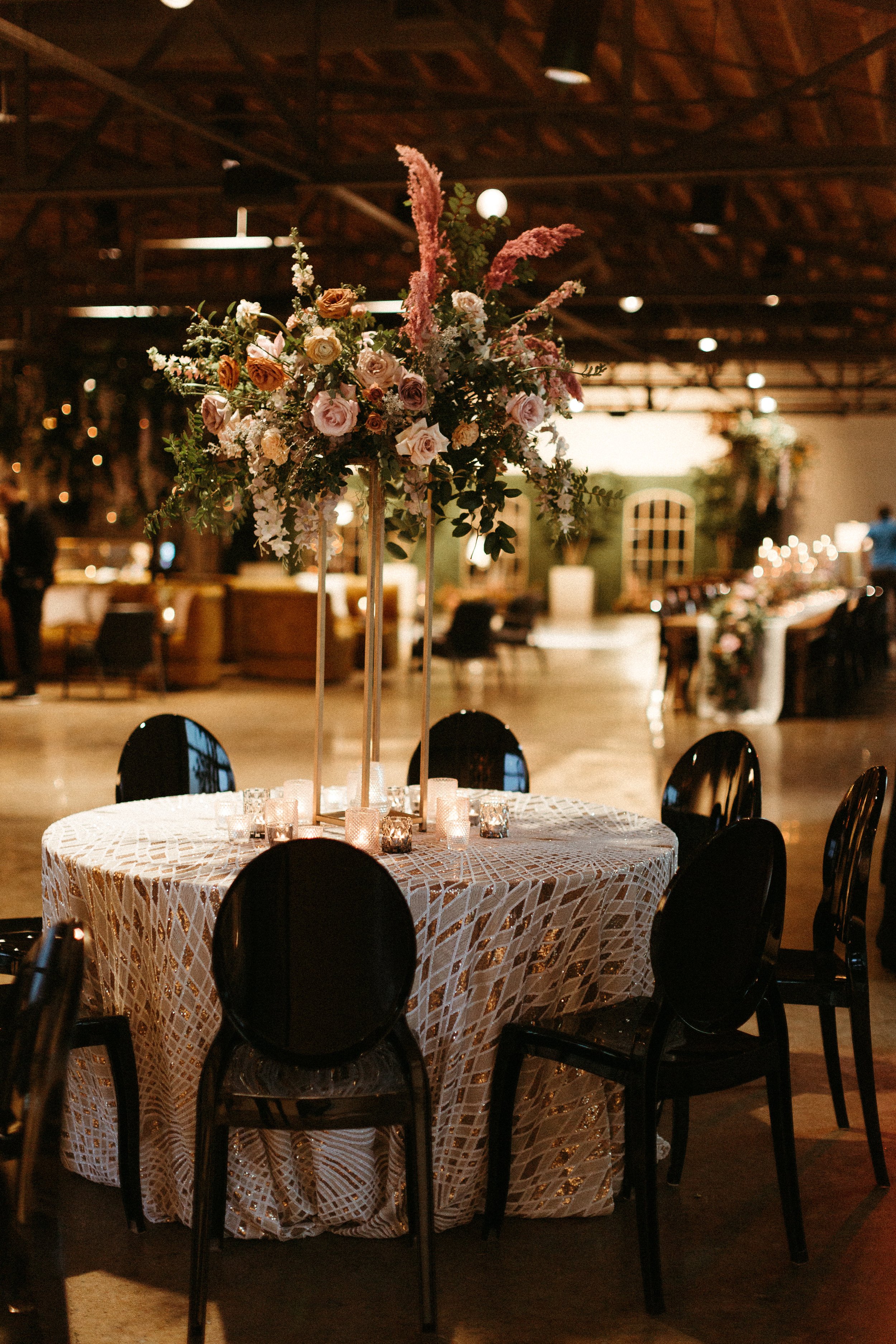 Stunning elevated centerpieces decorate this art deco wedding. Floral hues of terra cotta, mauve, burgundy, and dusty pink are brought to life with petal heavy roses, dried branches, and pink pampas grass. Designed by Rosemary and Finch in Nashville,