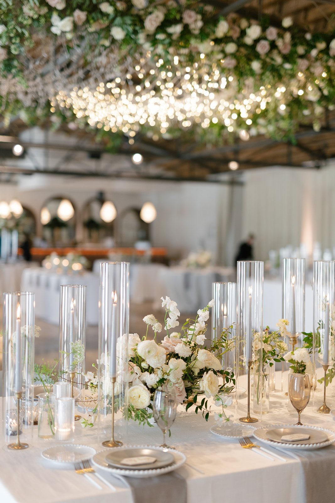 Low floral centerpieces for elegant wedding overflowing with white garden roses, ranunculus, butterfly ranunculus, scabiosa, lisianthus, sweet peas, and natural dark greenery. Floral hues of white, cream, and blush. Designed by Rosemary and Finch in