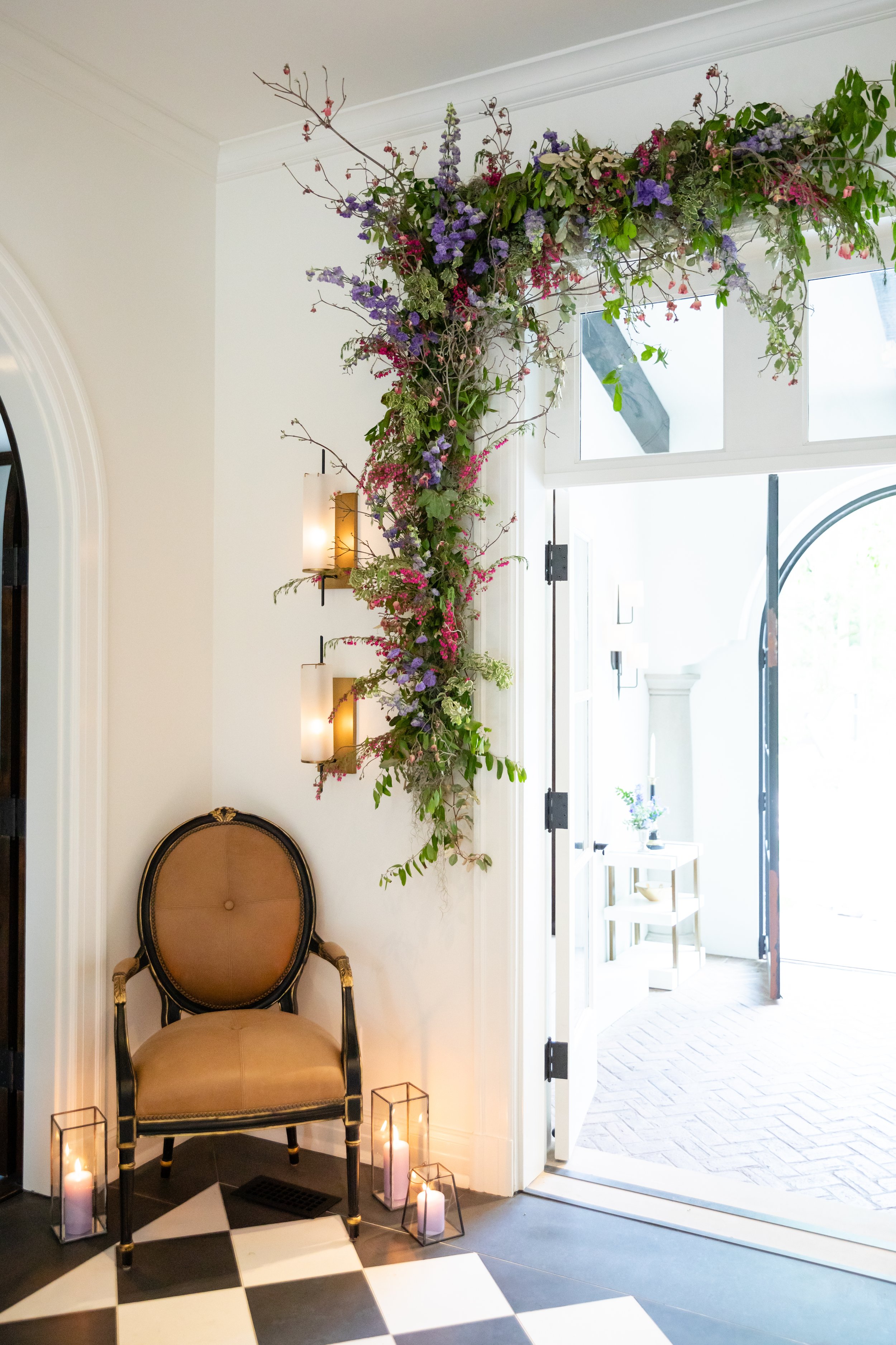 Lush floral installation growing to frame the doorway arch with natural greenery, purple globe allium, blush garden roses, and pastel wildflowers. Bridgerton inspired engagement party at a private home in Nashville, TN.