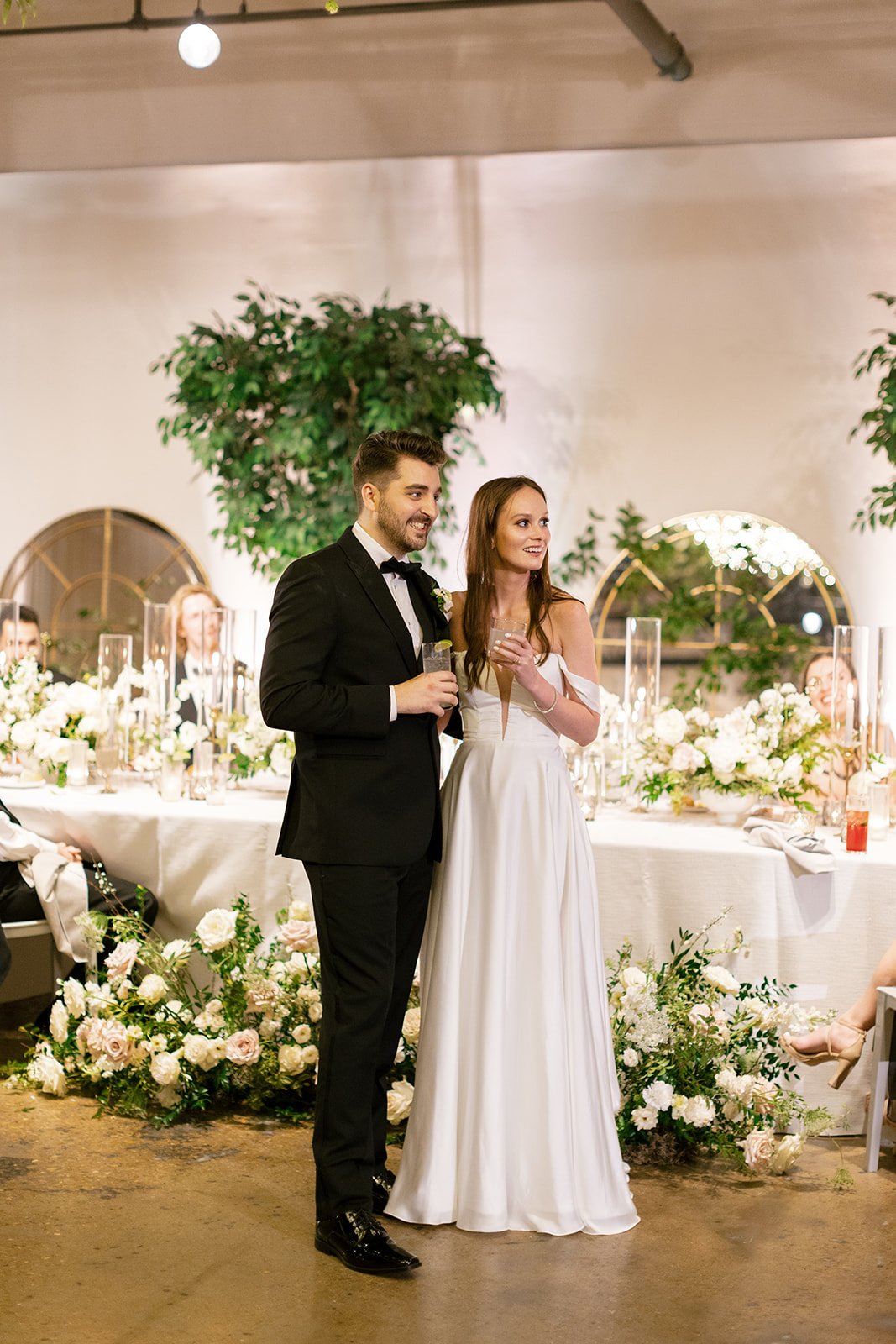 Low floral centerpieces for elegant wedding overflowing with white garden roses, ranunculus, butterfly ranunculus, scabiosa, lisianthus, sweet peas, and natural dark greenery. Floral hues of white, cream, and blush. Designed by Rosemary and Finch in