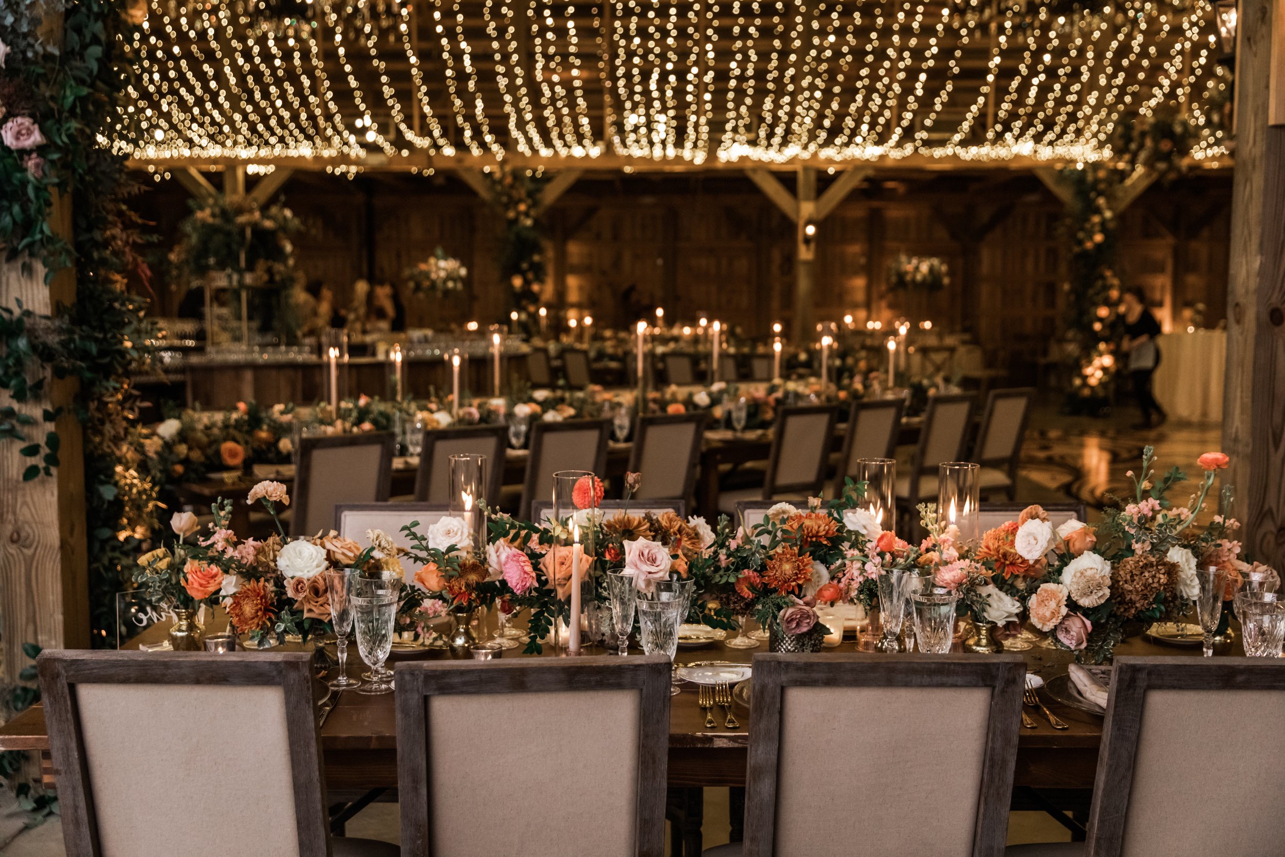 Beautiful fall floral centerpieces warm this reception space with a sunset color palette. Garden roses, ranunculus, double brownie tulips, and lisianthus create hues of terra cotta, blush pink, copper, and yellow. Designed by Rosemary and Finch in Na