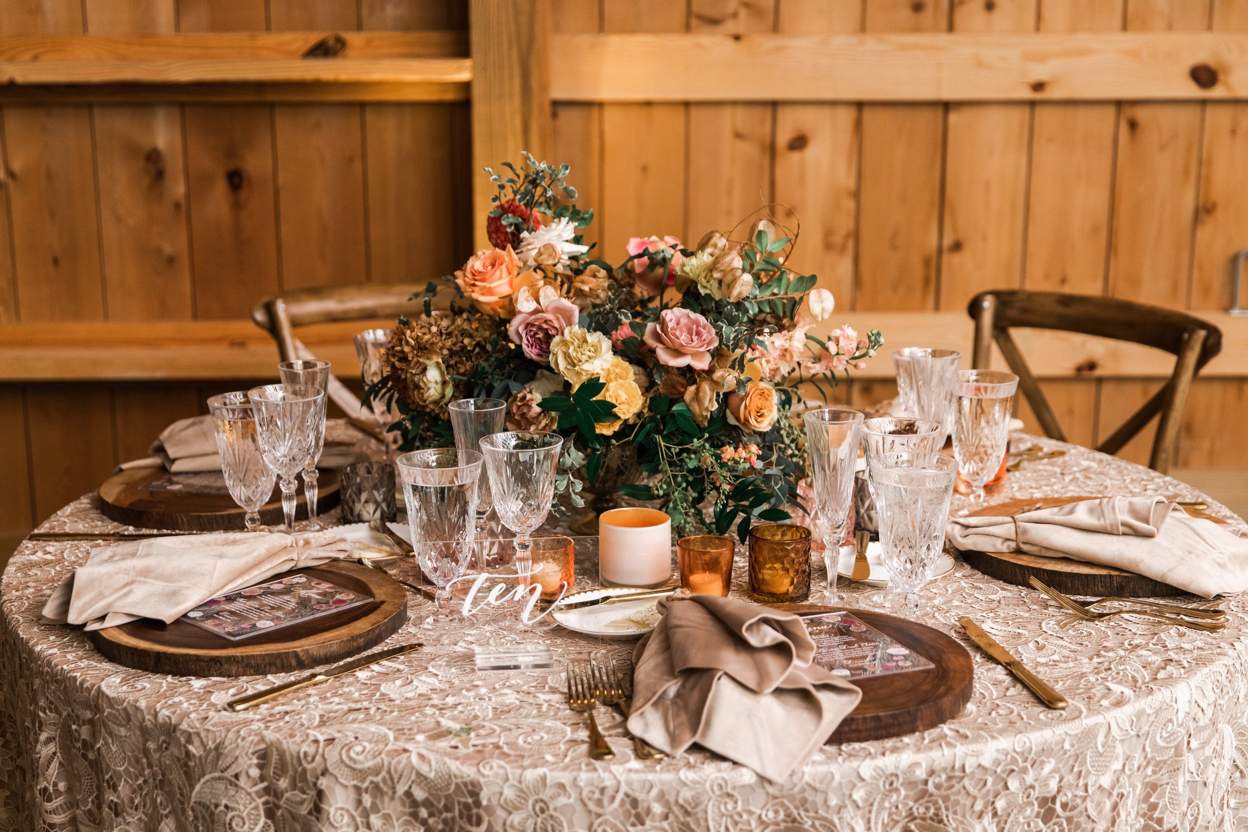 Beautiful fall floral centerpieces warm this reception space with a sunset color palette. Garden roses, ranunculus, double brownie tulips, and lisianthus create hues of terra cotta, blush pink, copper, and yellow. Designed by Rosemary and Finch in Na