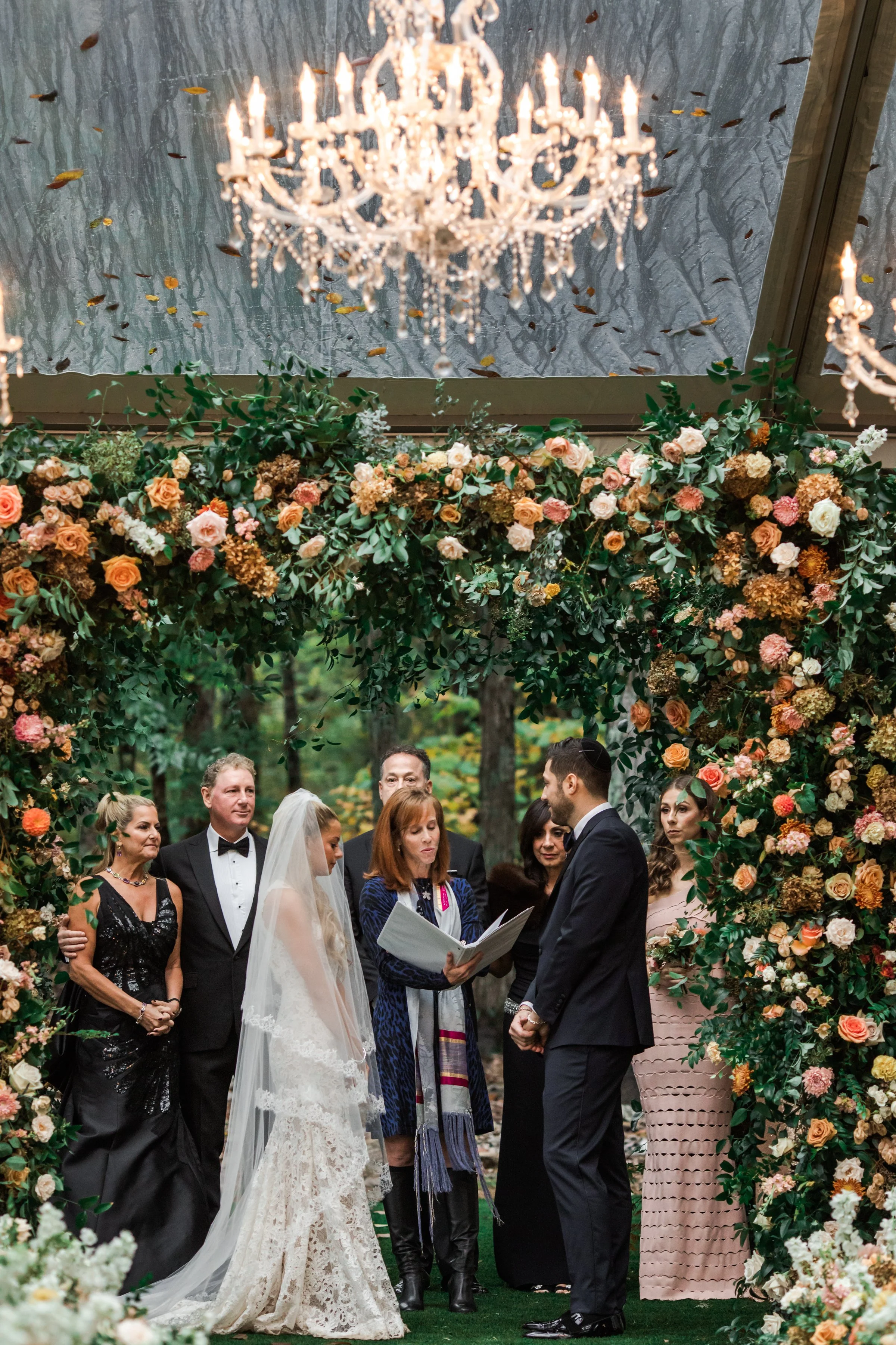 Eye-catching oversized chuppah overflowing with fall florals featuring dahlias, garden roses, rain tree pods, and fall greenery. Autumnal hues of terra cotta, dusty pink, copper, and yellow create this statement wedding piece. Designed by Rosemary an
