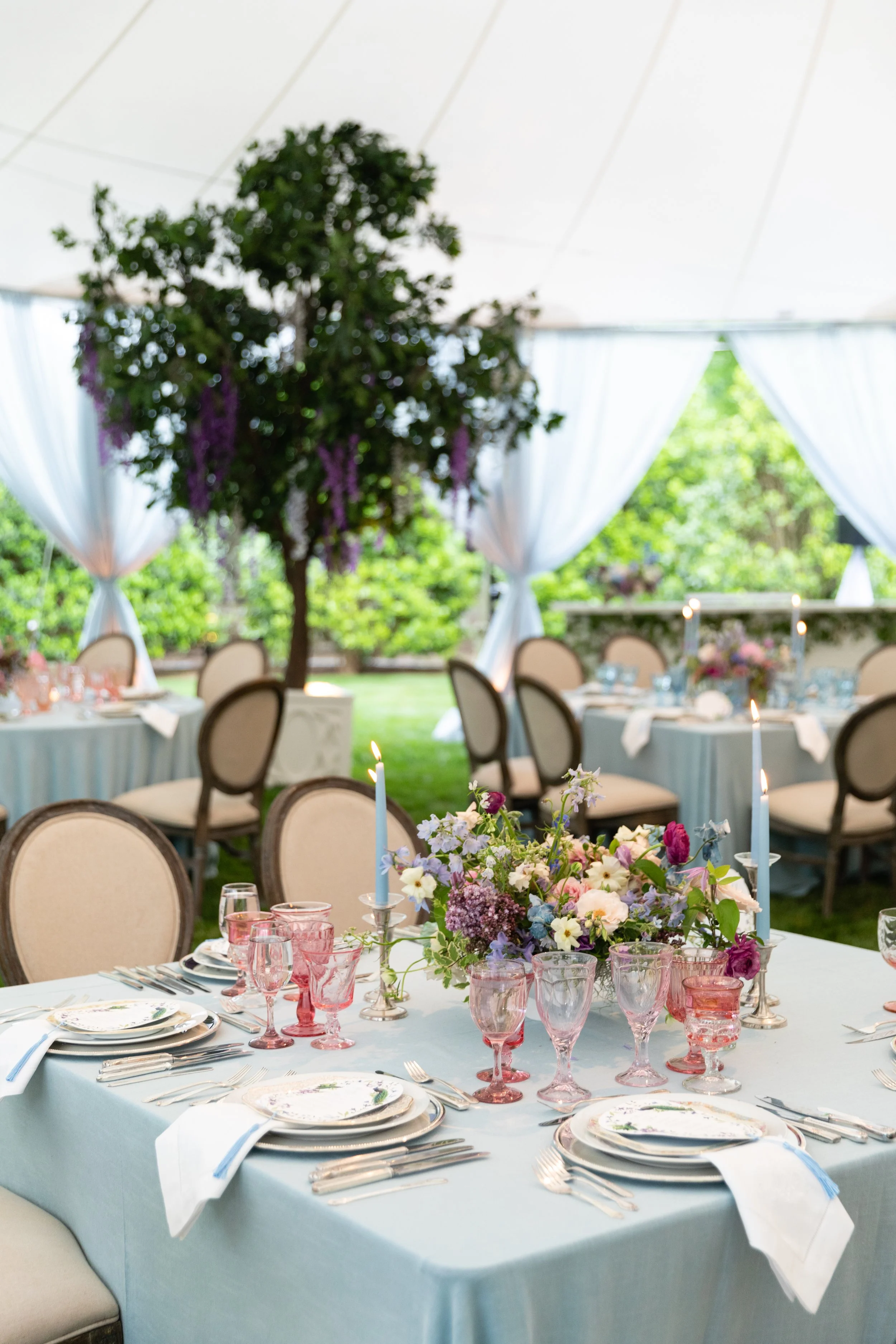 Growing, fresh floral centerpieces with blush garden roses, lilac, blue sweet peas, ranunculus, lavender delphinium, globe allium, clematis, and natural greenery for a tented Bridgerton inspired engagement party at a private home in Nashville, TN.