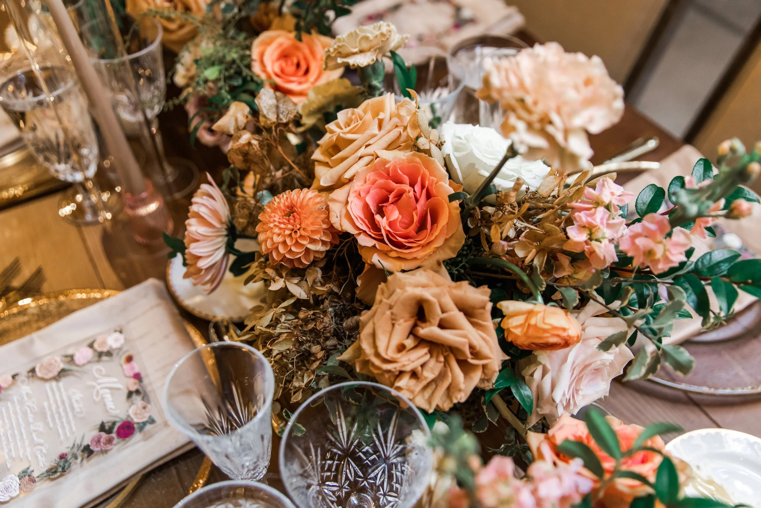 Beautiful fall floral centerpieces warm this reception space with a sunset color palette. Garden roses, ranunculus, double brownie tulips, and lisianthus create hues of terra cotta, blush pink, copper, and yellow. Designed by Rosemary and Finch in Na