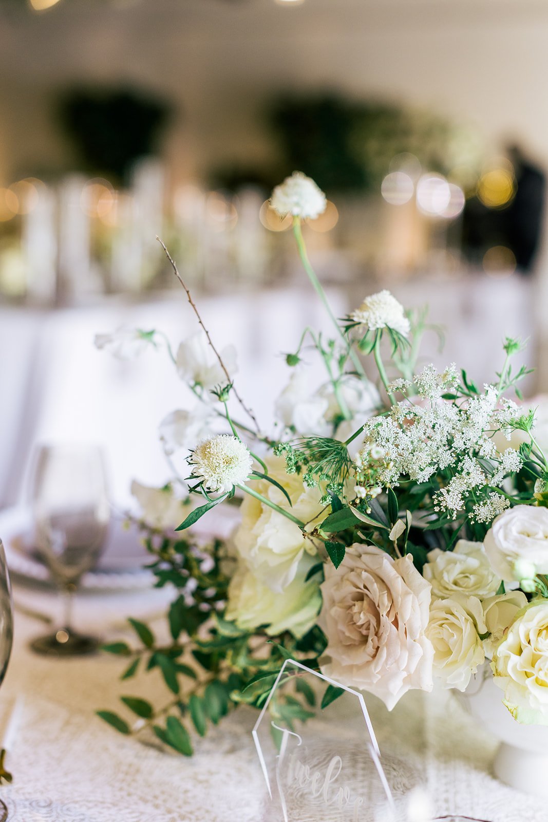 Low floral centerpieces for elegant wedding overflowing with white garden roses, ranunculus, butterfly ranunculus, scabiosa, lisianthus, sweet peas, and natural dark greenery. Floral hues of white, cream, and blush. Designed by Rosemary and Finch in