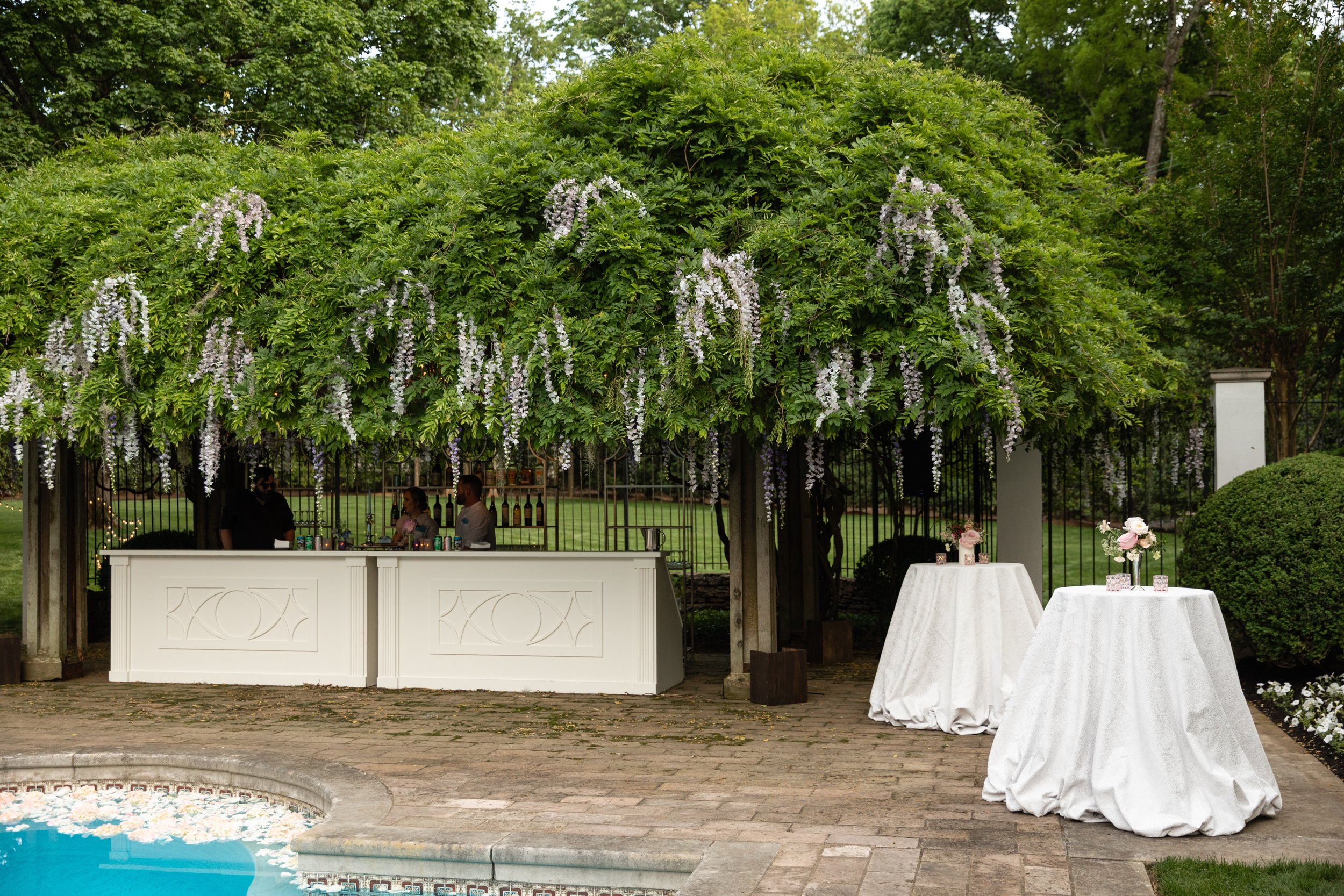 Bridgerton inspired engagement party at a private home in Nashville, TN with pastel candles and flowers floating in the pool with wisteria and delphinium growing over the bar. Nashville wedding floral designer, Rosemary & Finch.